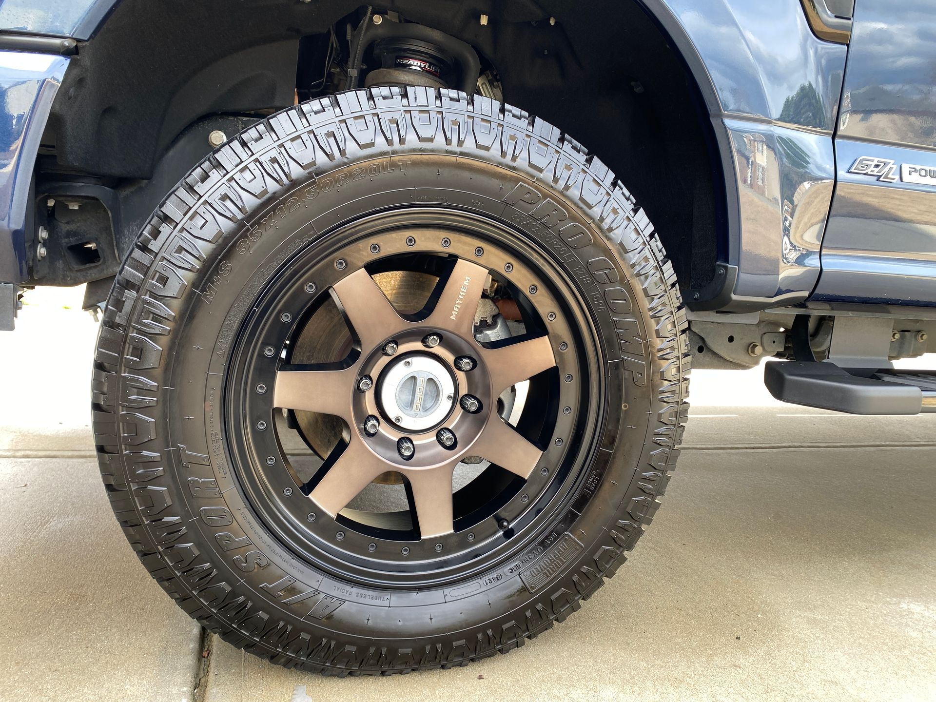 Close-up of a blue truck tire with a bronze-colored rim and rugged, black tread.