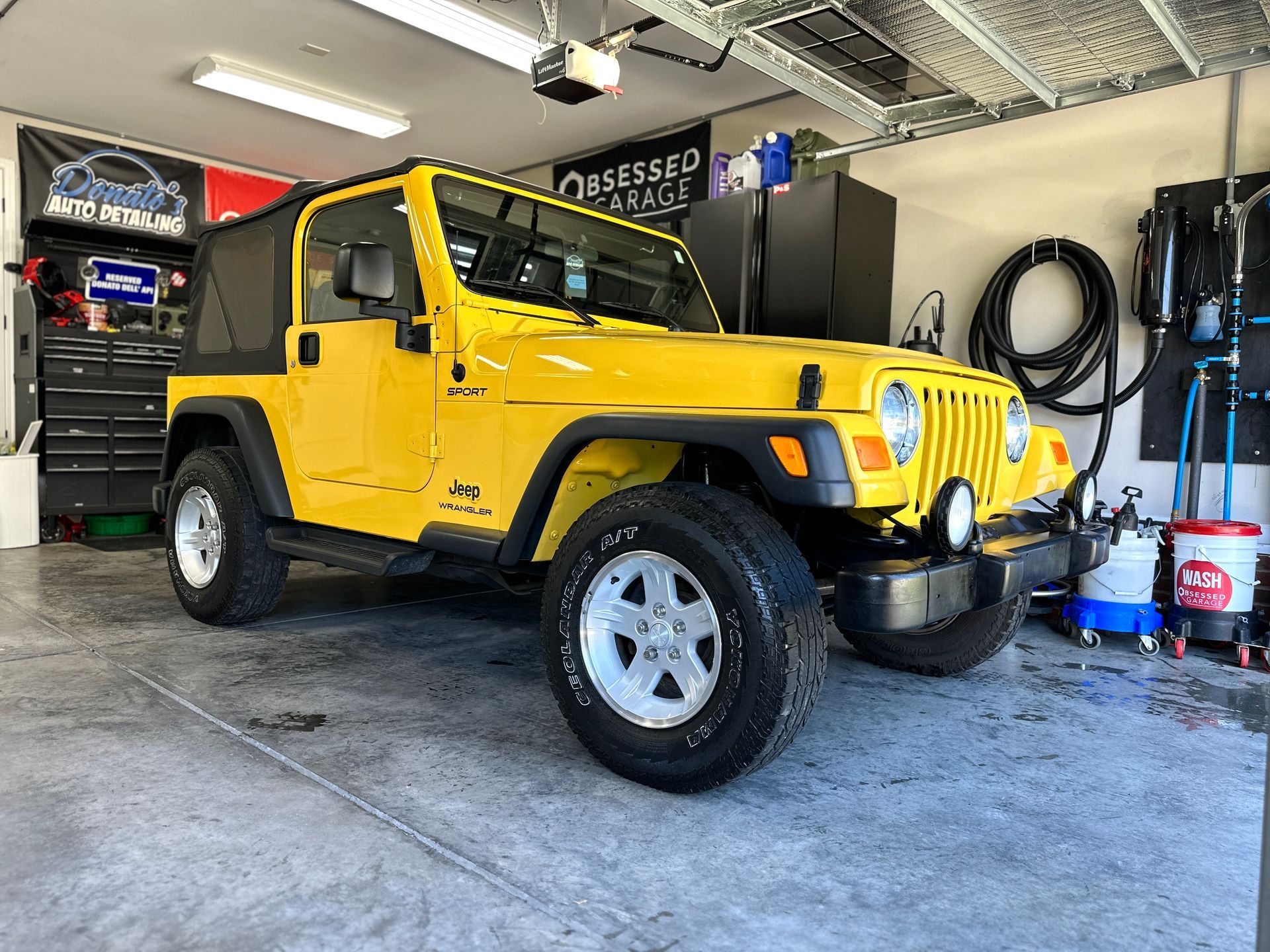 Yellow Jeep Wrangler parked inside a well-lit garage with detailing equipment.