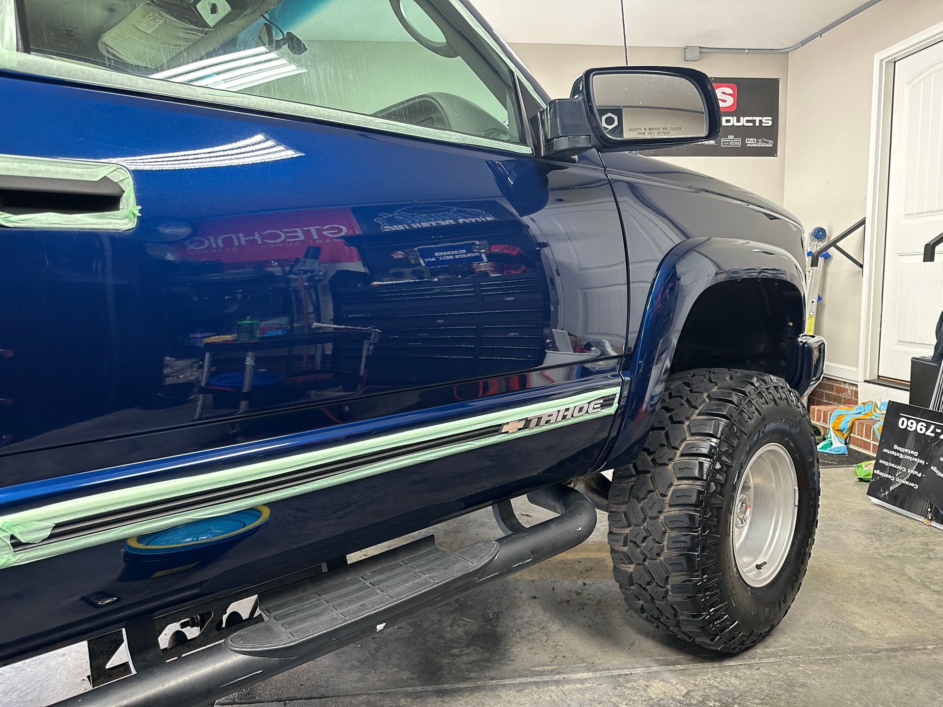 Blue pickup truck with lifted suspension and custom wheels, parked indoors.