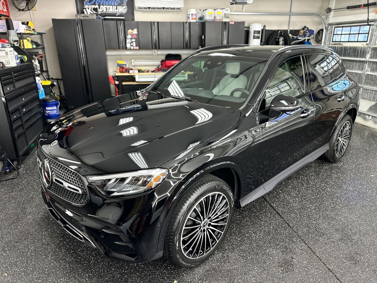 Black Mercedes SUV parked in a garage with black cabinets and speckled flooring.