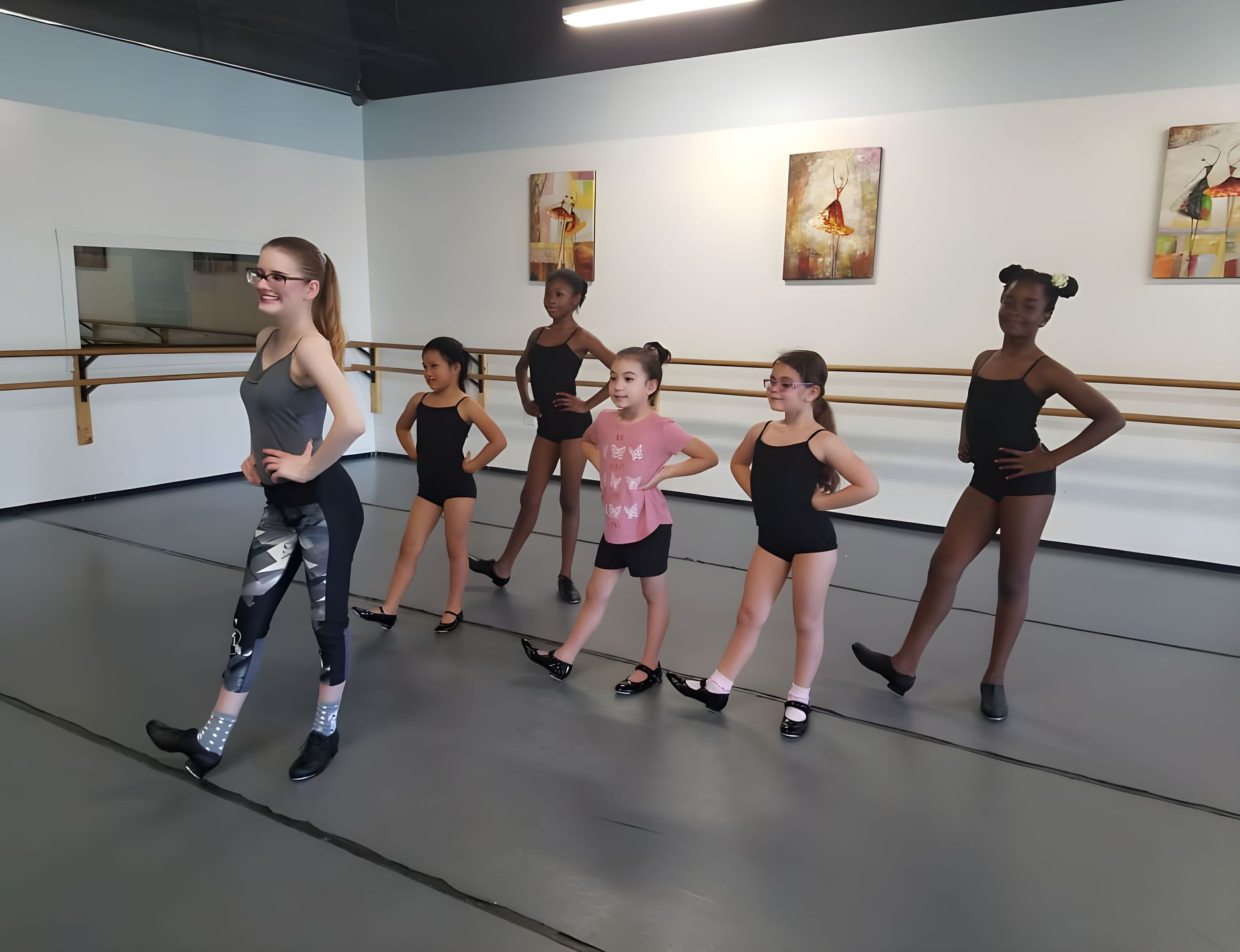 Tap class: Instructor with a ponytail leads five young girls in a studio.