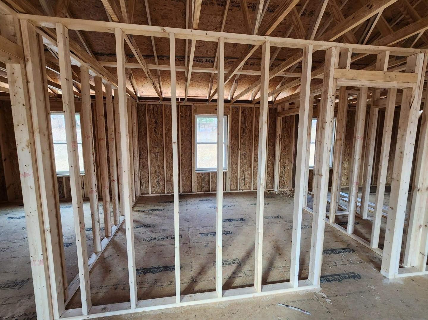 Interior of a house under construction; wooden studs frame walls, windows, and ceiling.