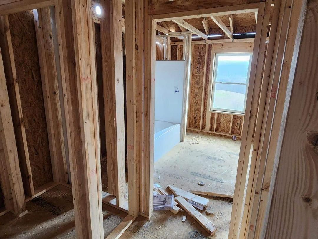 Interior view of a bathroom under construction, showing wooden framing and a window.
