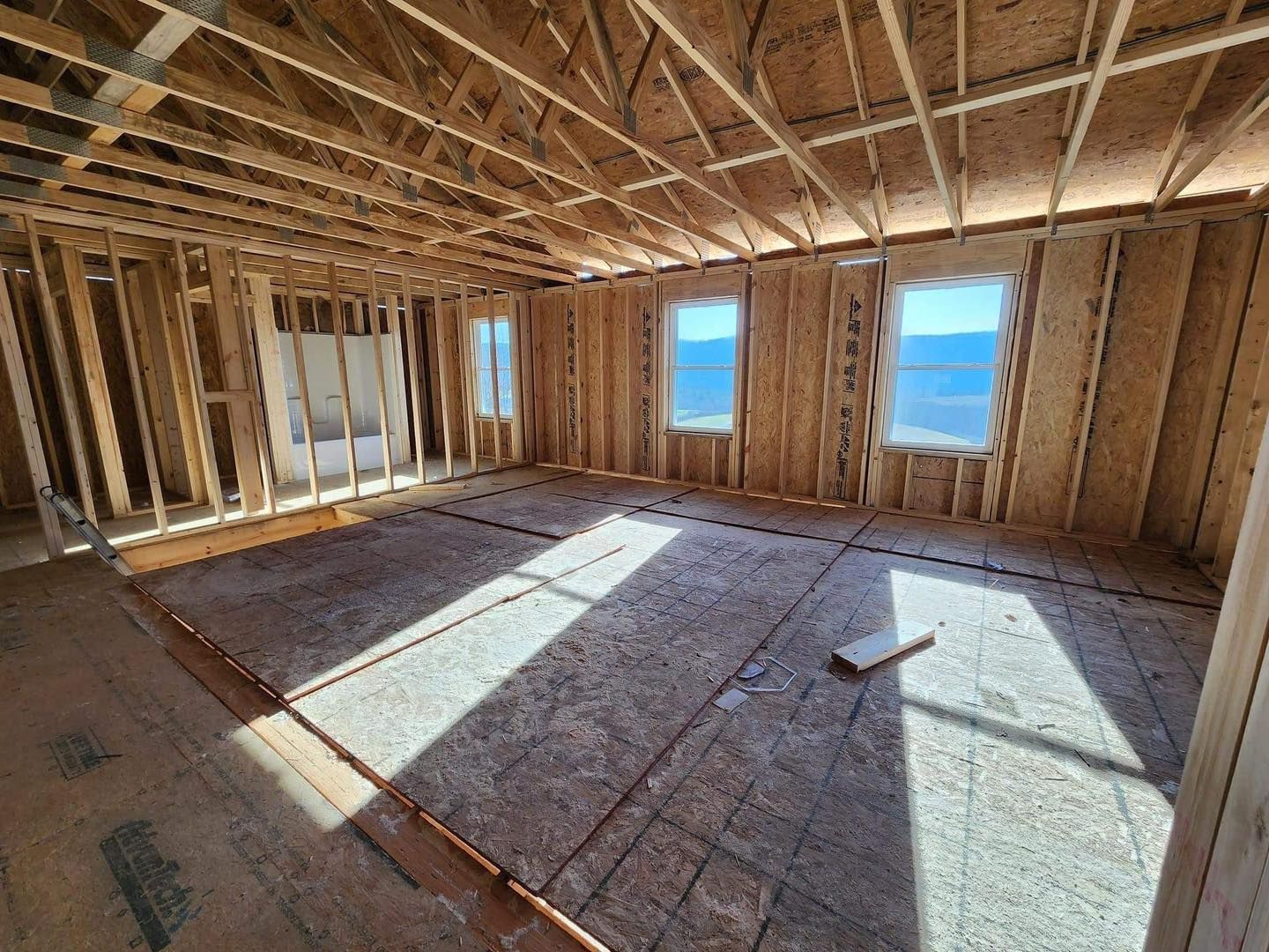 Interior of a room under construction, with wooden framing, windows, and exposed flooring.