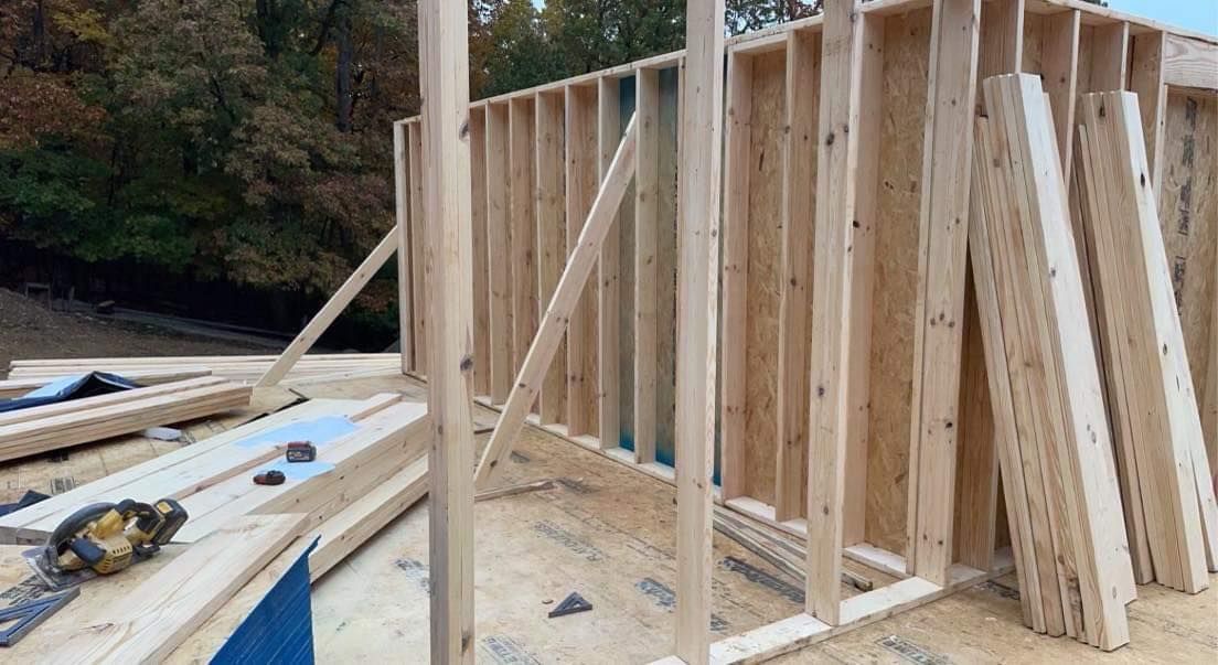 Wooden house frame under construction outdoors with supporting beams and lumber.
