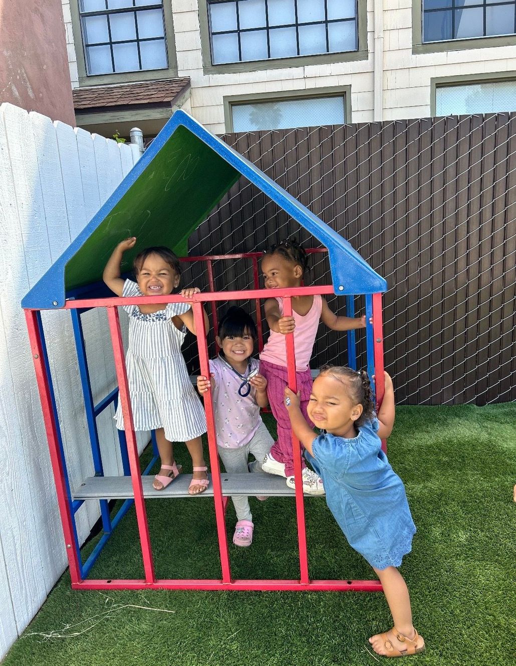 Three children playing inside a colorful backyard playhouse, smiling and posing at the doorway