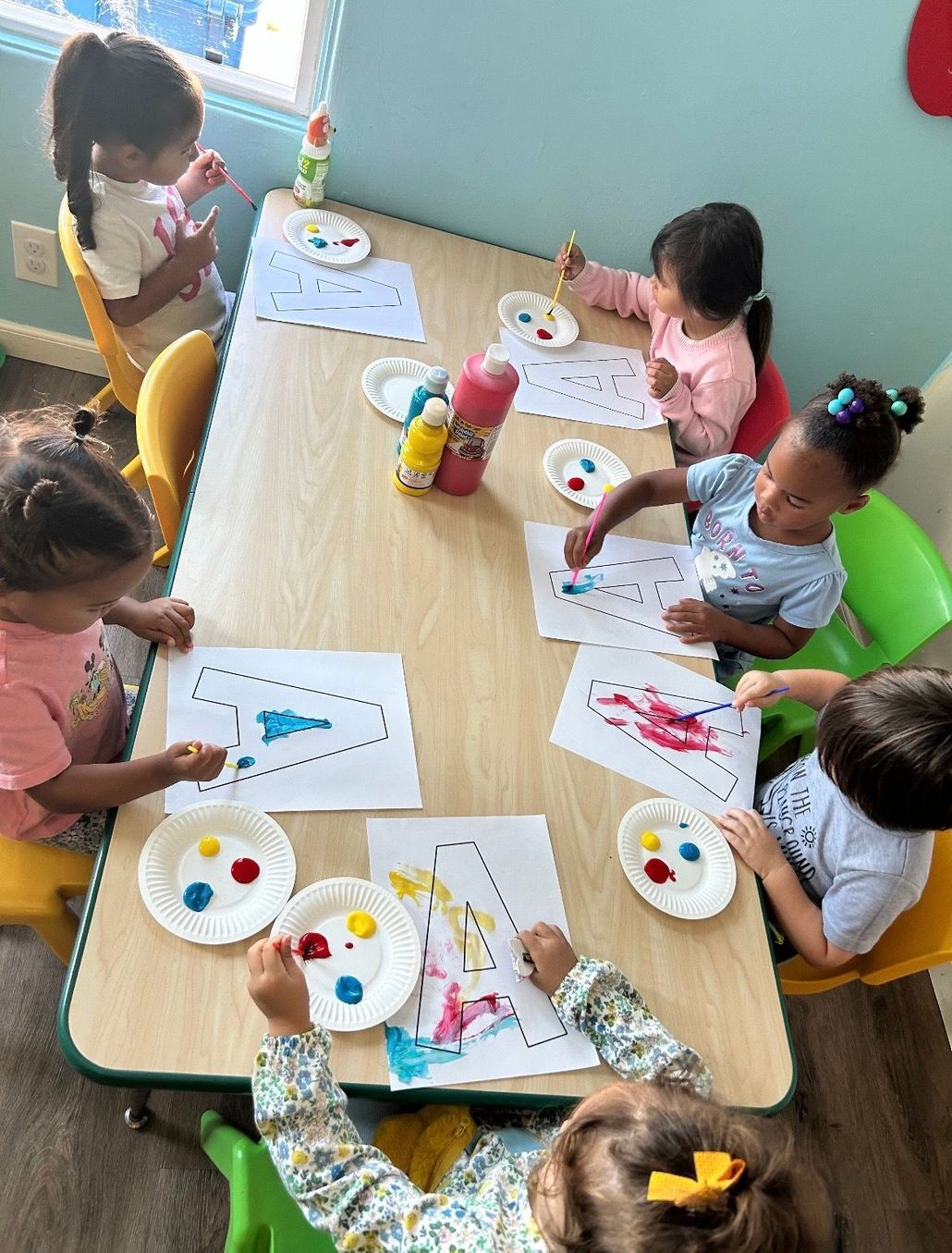 Three children playing with stacking rings and blocks at a colorful table.