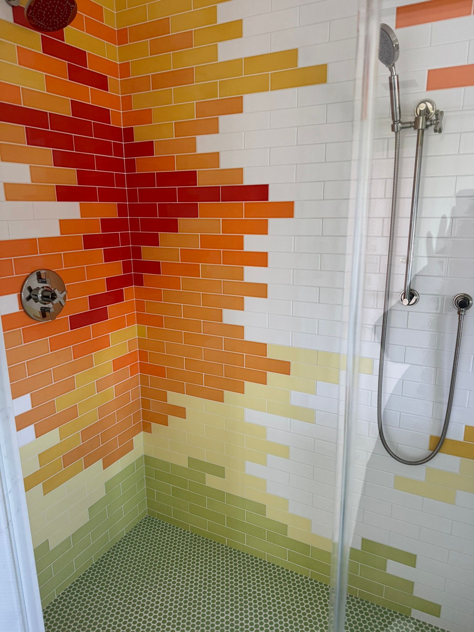 Shower with colorful brick-style tile design transitioning from green to yellow to orange and red.