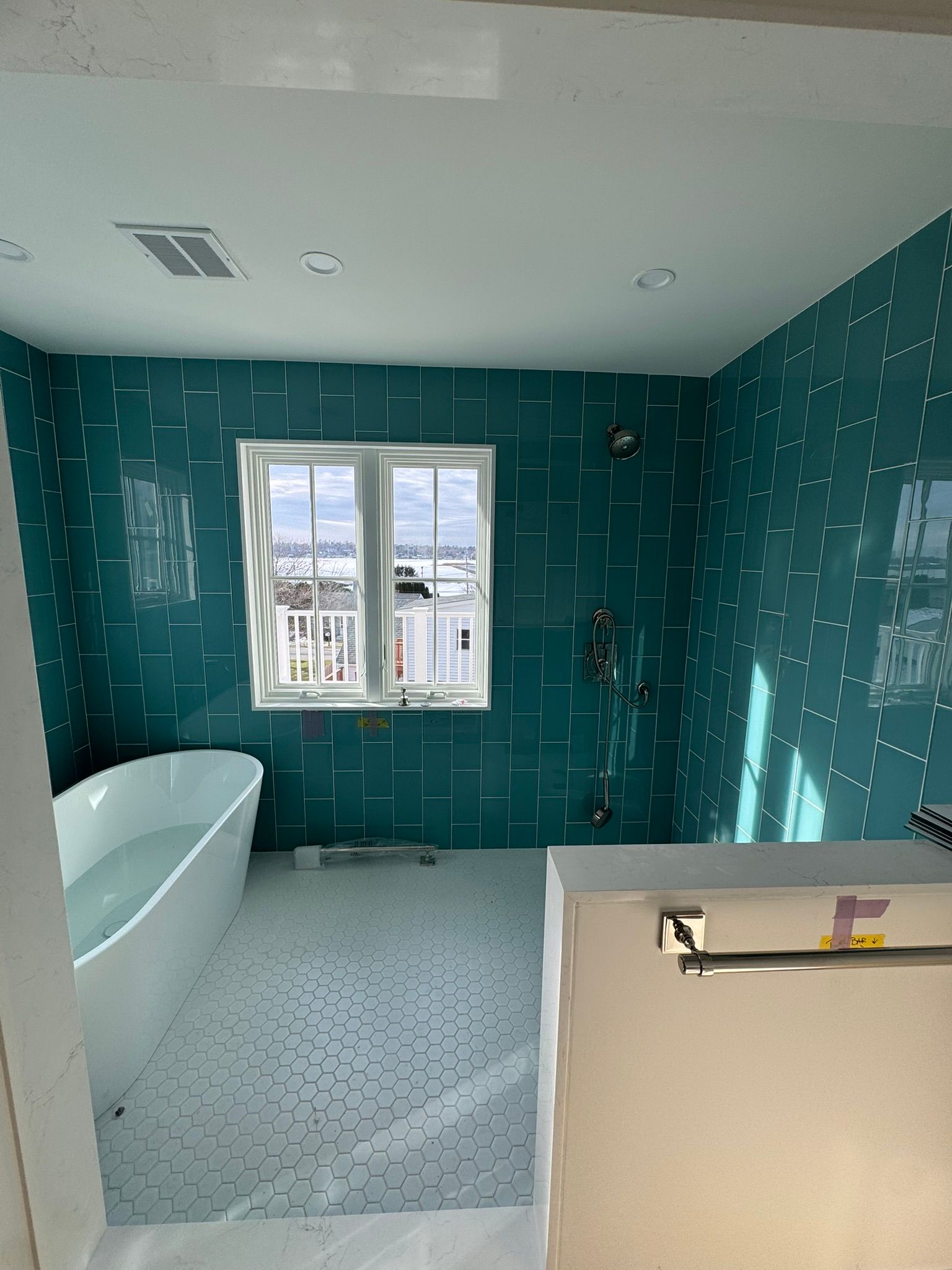 Teal-tiled bathroom with a freestanding tub, window, and shower fixtures.
