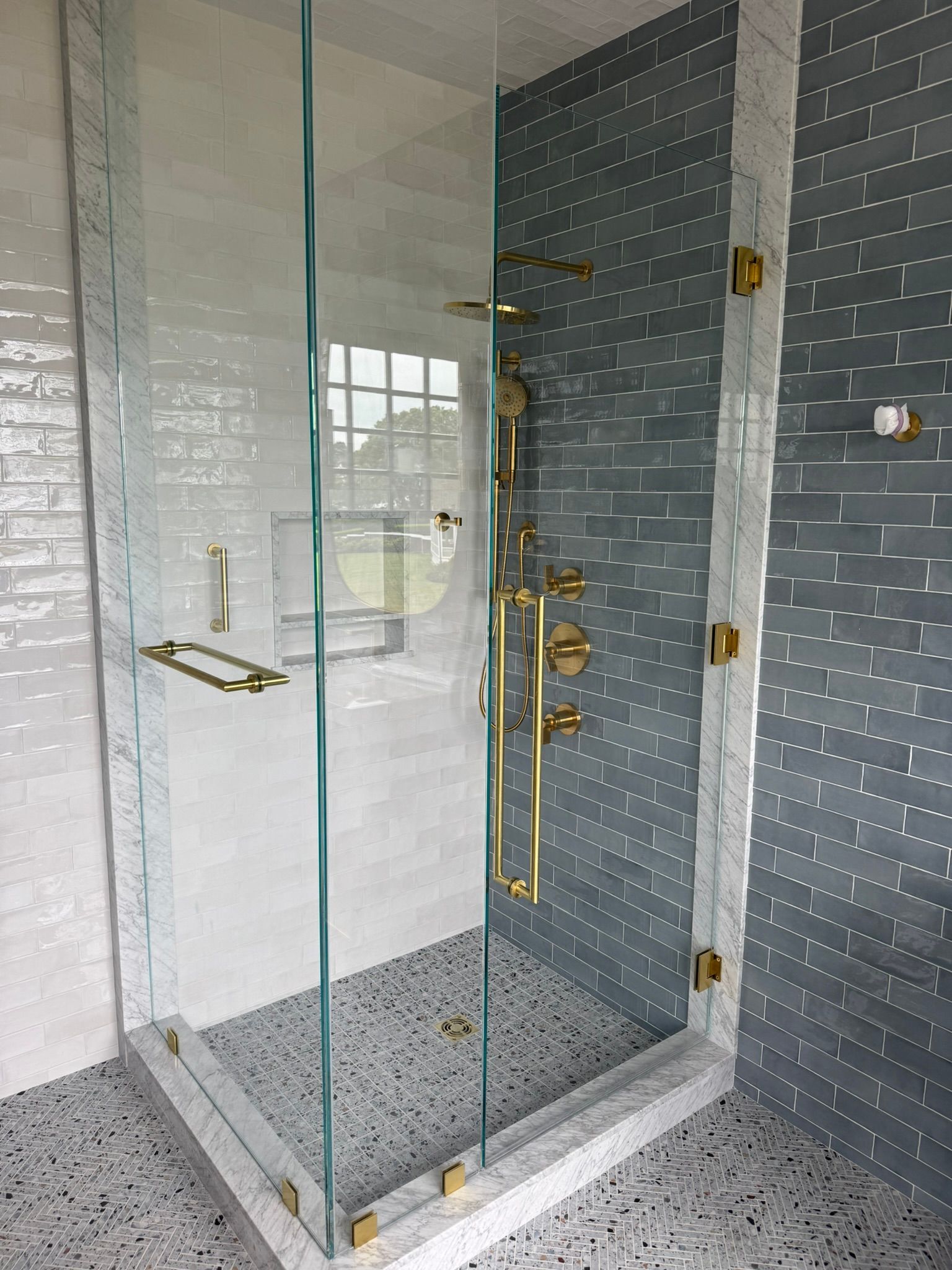 Glass-enclosed shower with gold fixtures and gray mosaic tile walls and floor.