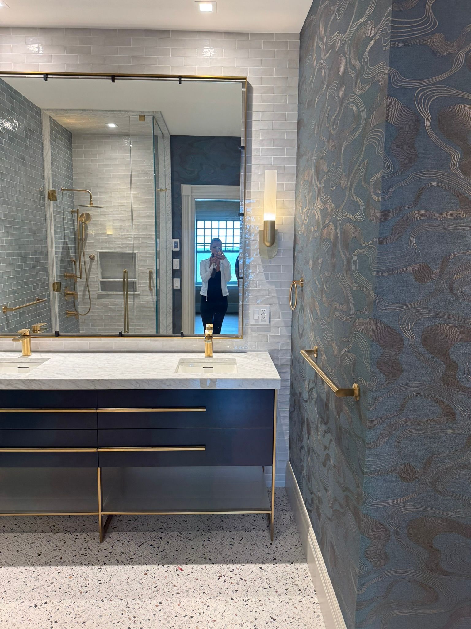 Luxurious bathroom with dark blue vanity, gold fixtures, marble countertop, and textured blue wall.