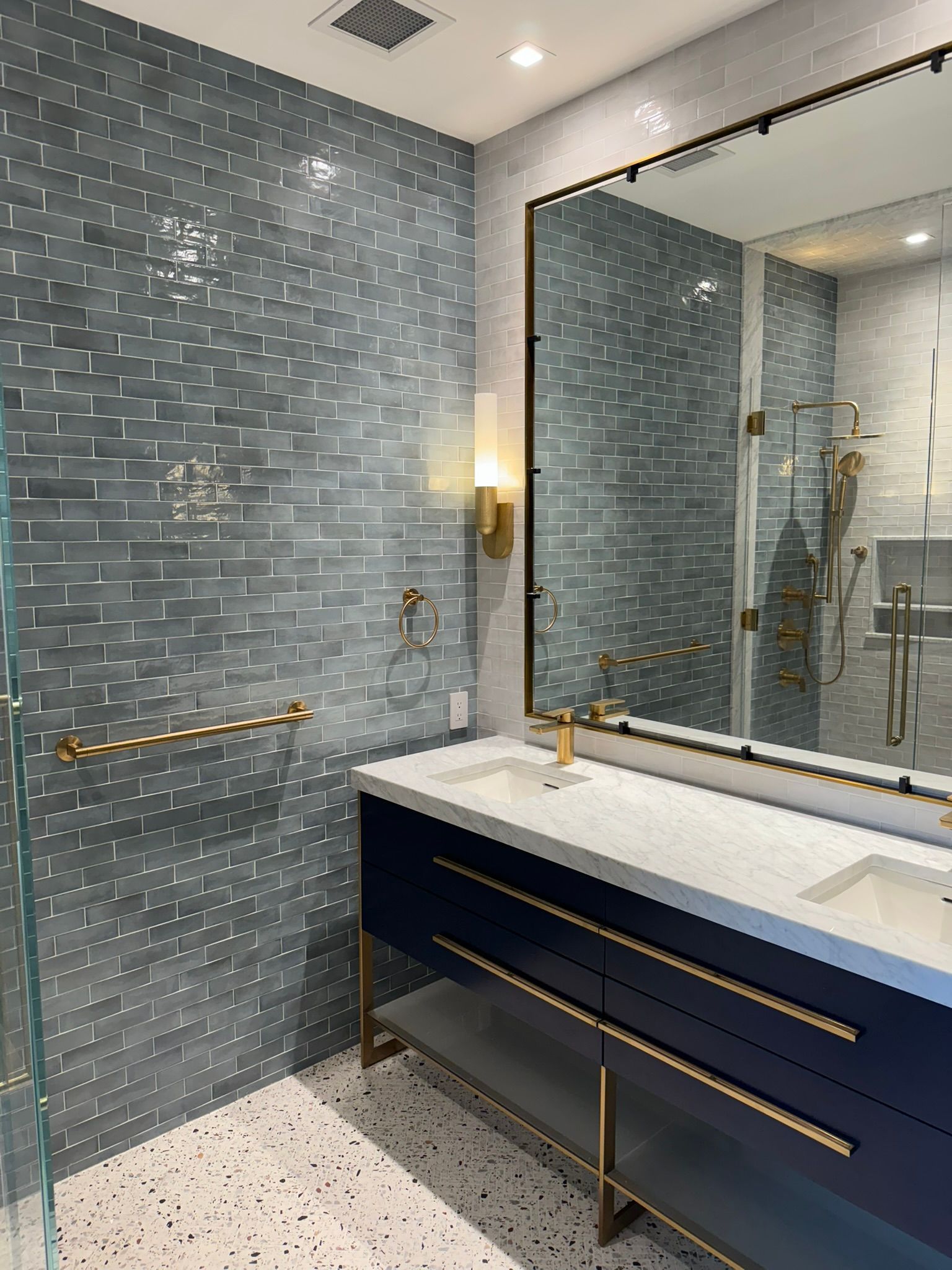 Blue tile bathroom with navy vanity, gold fixtures, and large mirror.