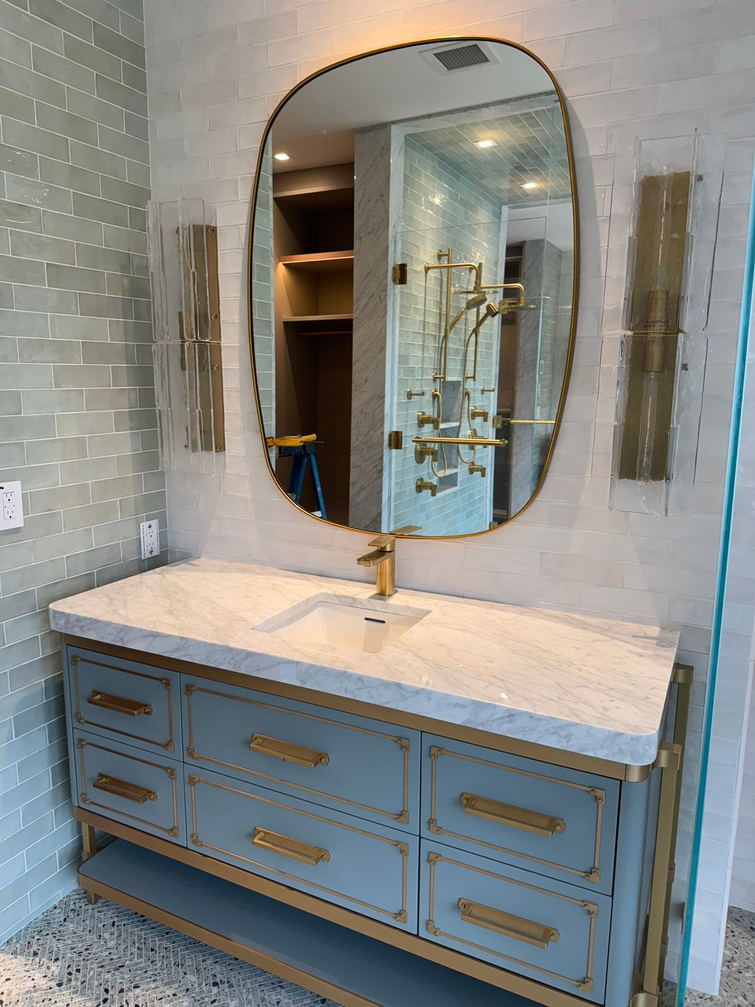 Bathroom vanity with oval mirror, gold accents, light blue cabinet, and white marble countertop.