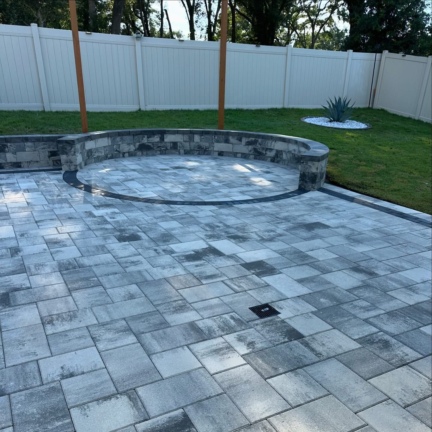 Backyard patio with paver stones, a raised circular fire pit, and a fenced lawn.