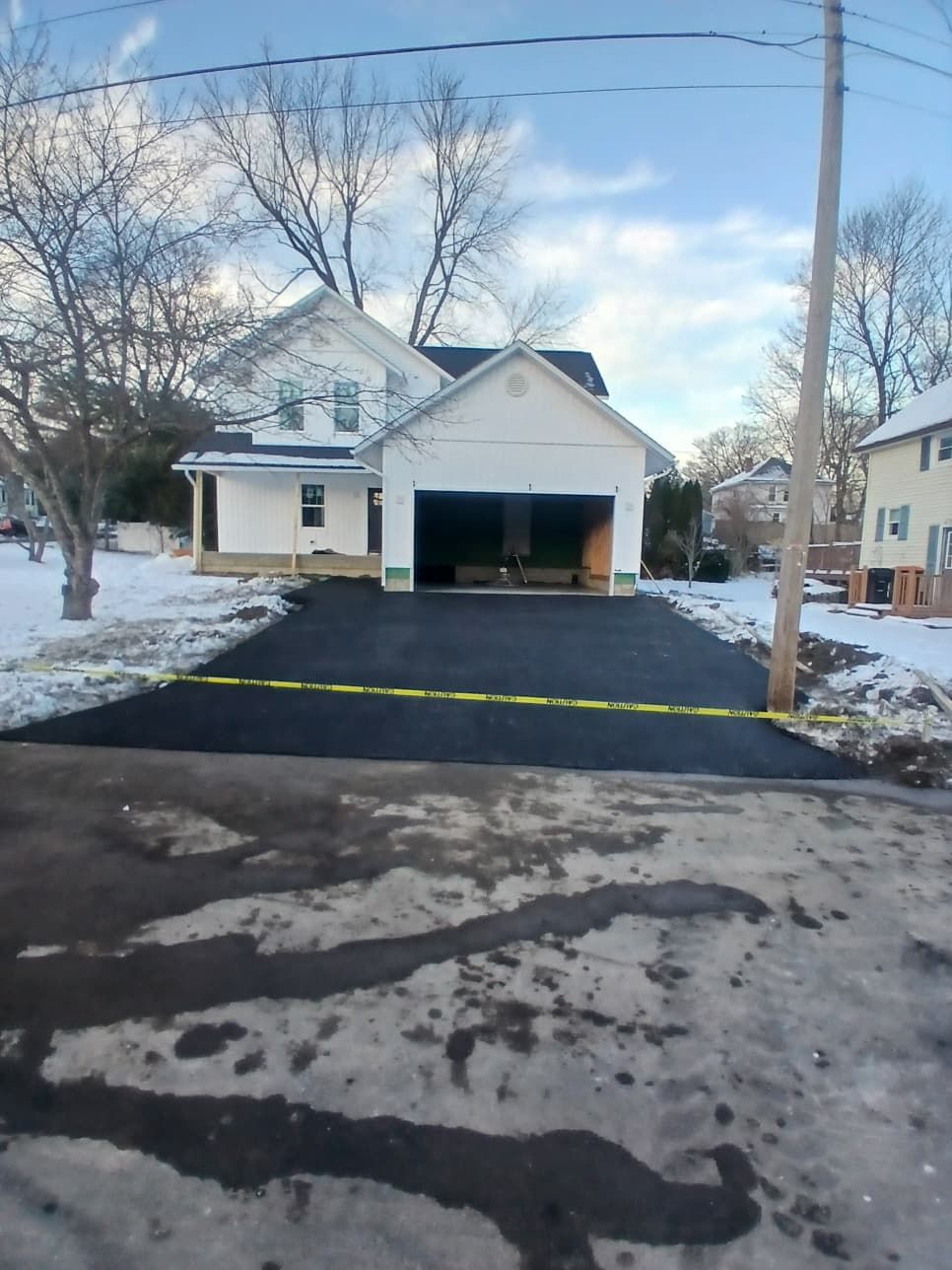 Snowy suburban house with an open garage and freshly paved black driveway