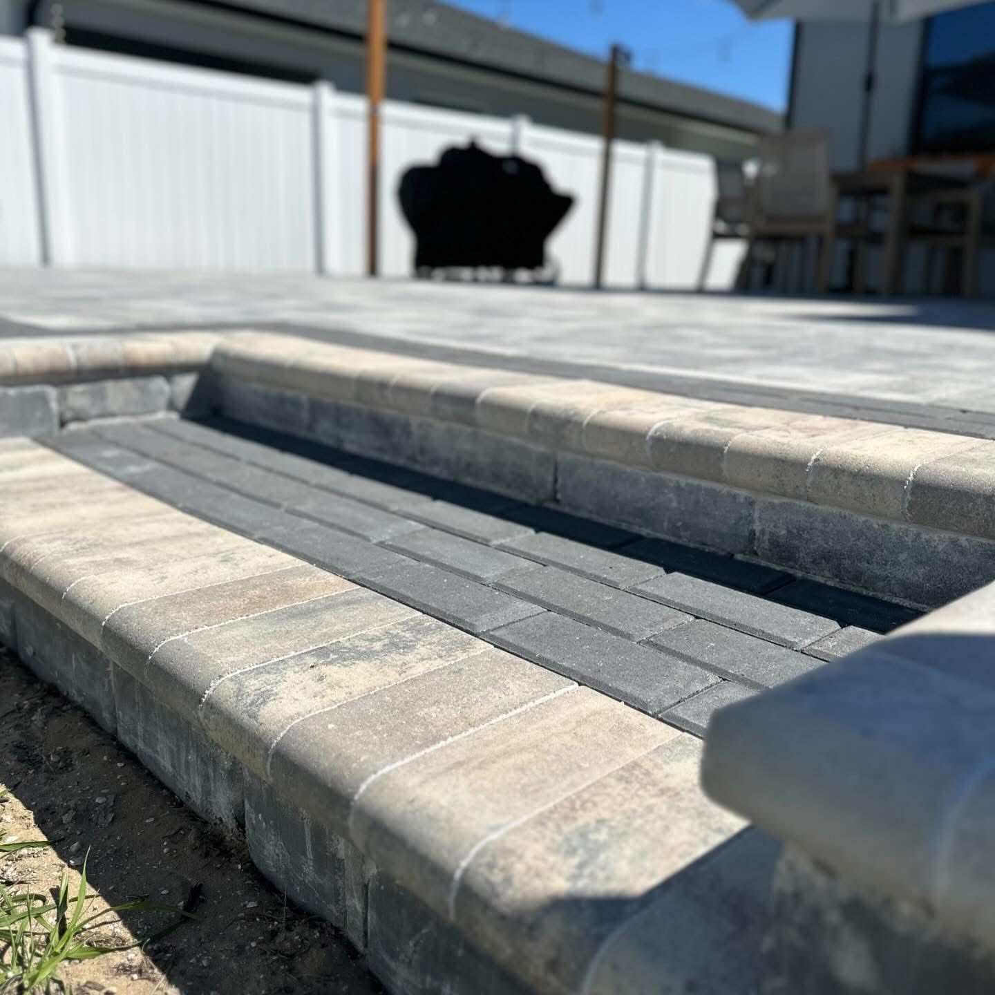 Stone steps leading to a patio with a white fence and building in bright sunlight