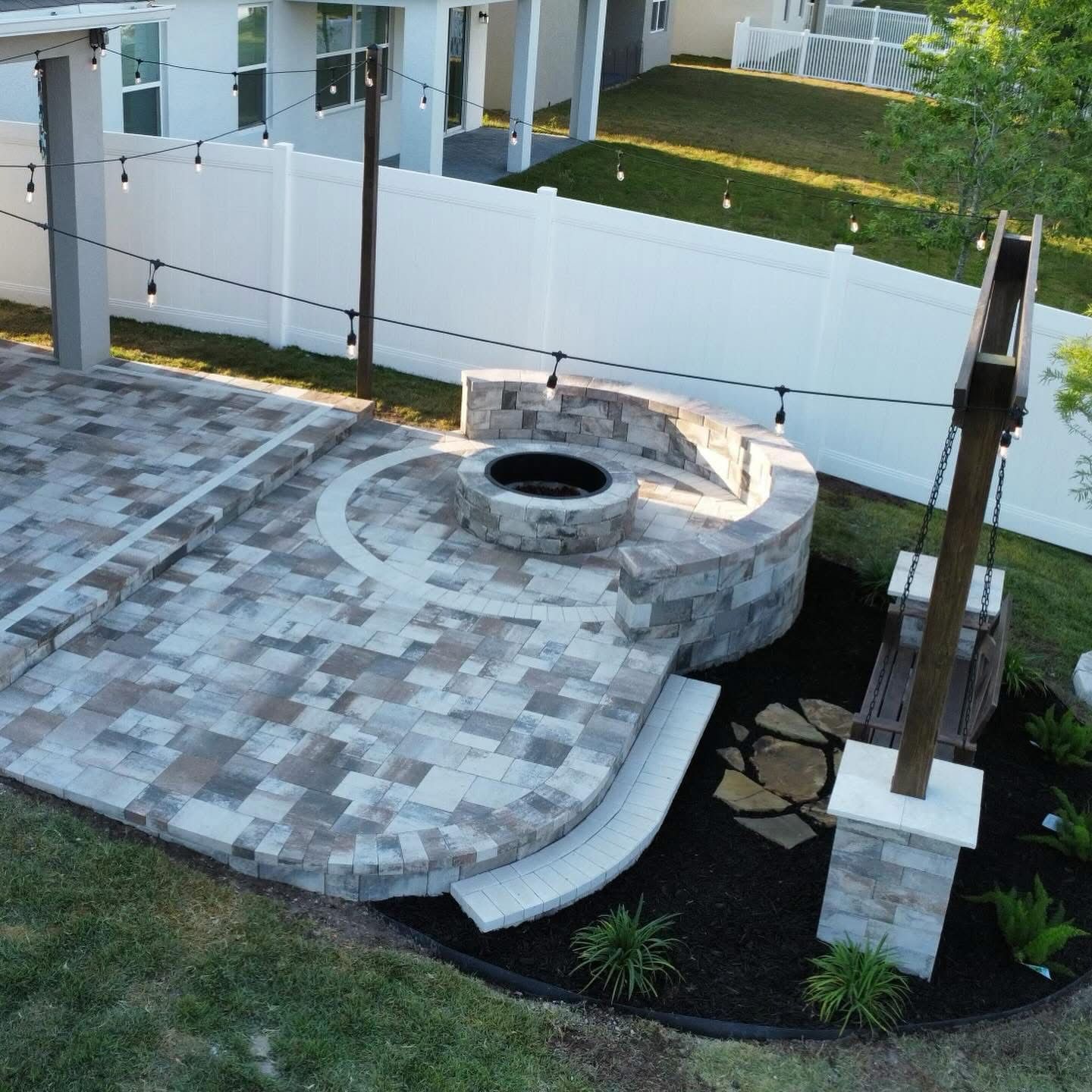 Backyard patio with tiled deck, round fire pit, white fence, and landscaped seating area
