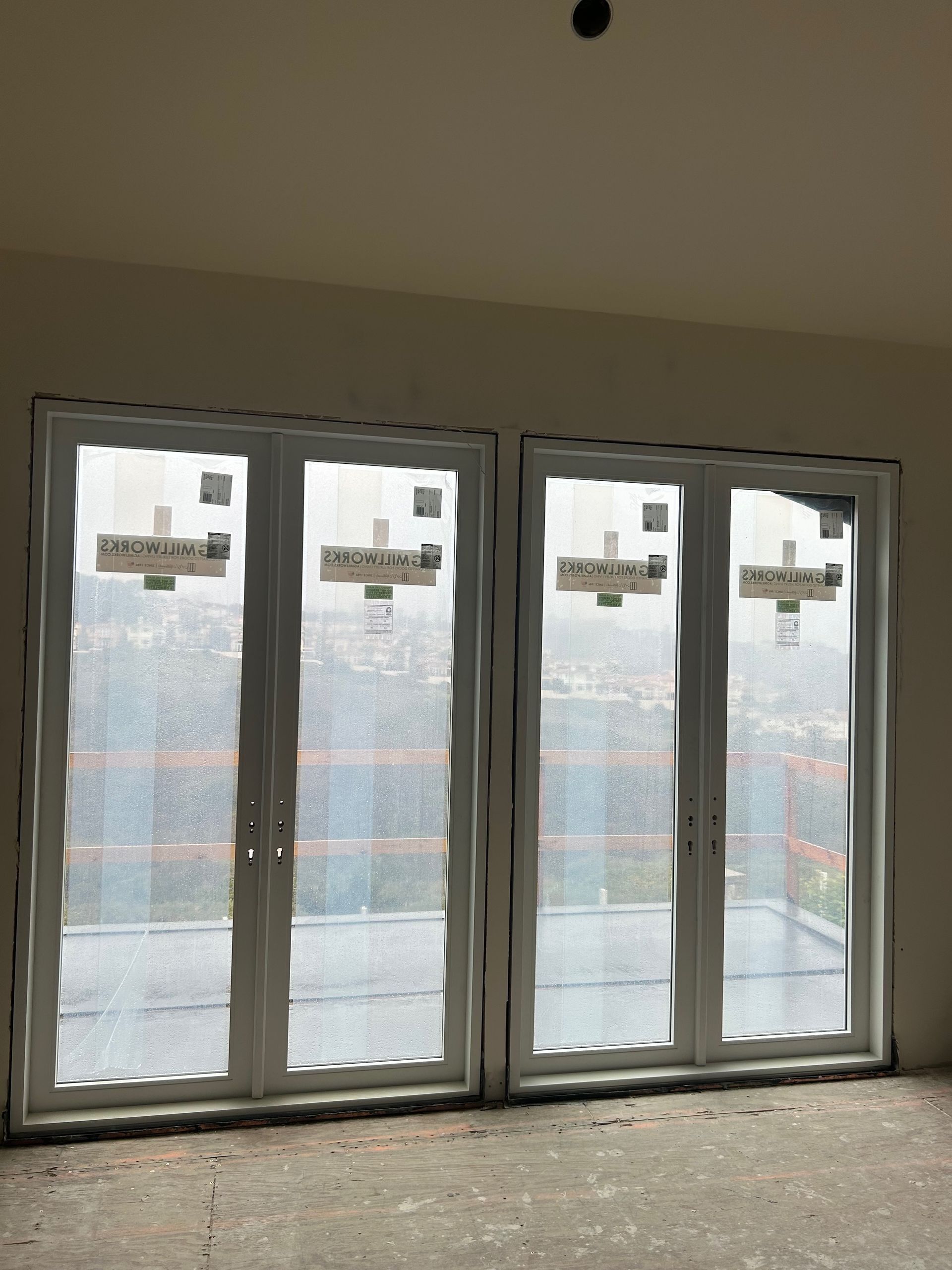 Two white-framed, multi-pane doors with protective covering, inside a room with unfinished walls.