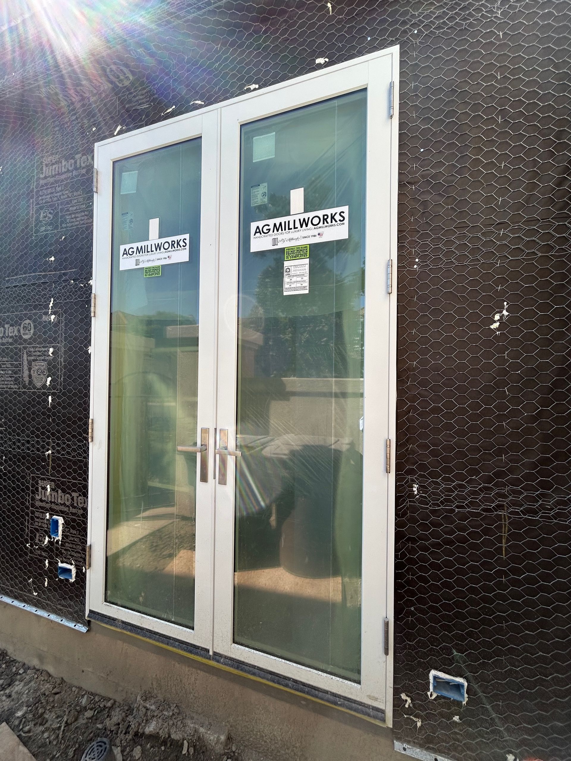 Double glass doors with white frame, on a building under construction, with a dark exterior surface.