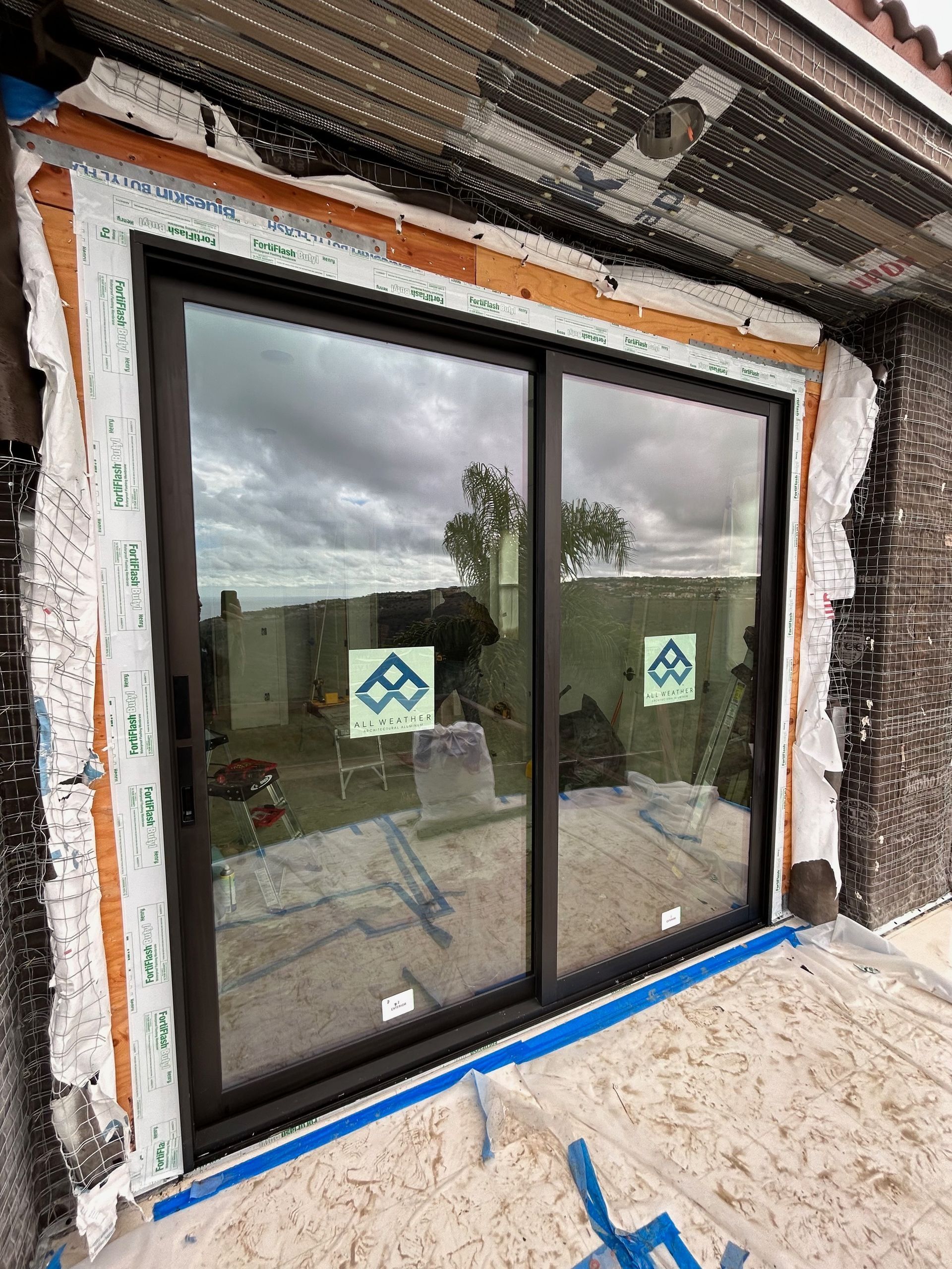 New dark-framed sliding glass door installed in a building's exterior wall, with weatherproofing and unfinished siding.