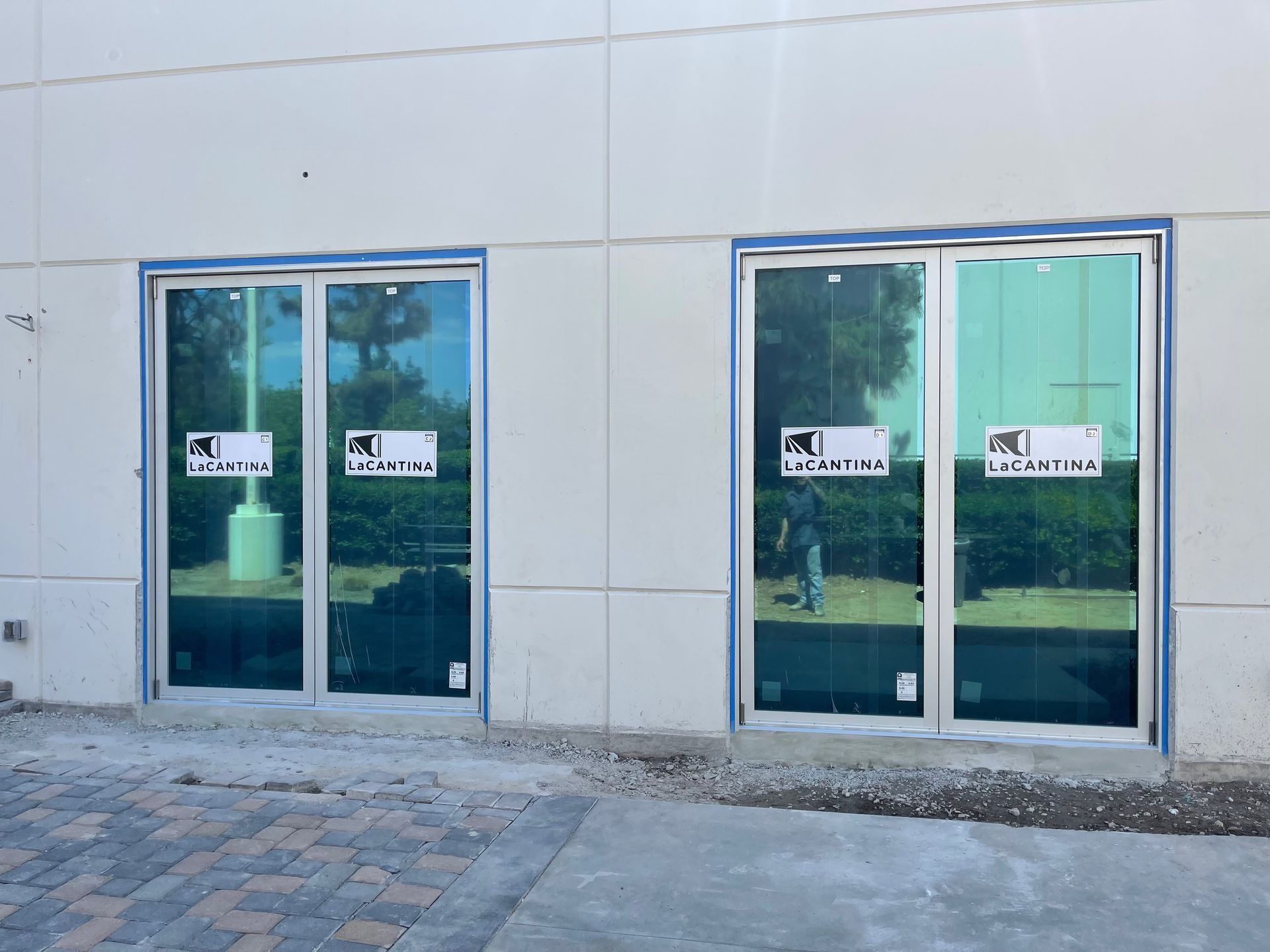 Two commercial glass doors with blue tape on a white building exterior.