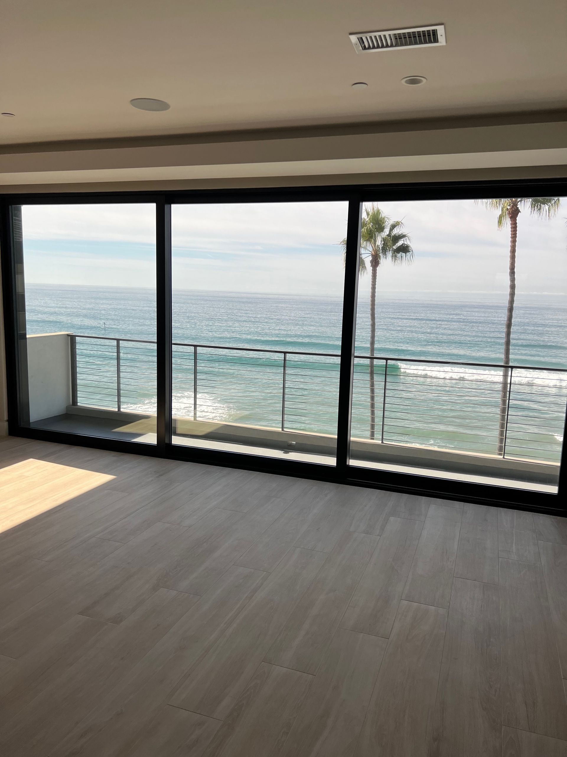 Ocean view through sliding glass doors in a modern room with wood floors and palm trees.