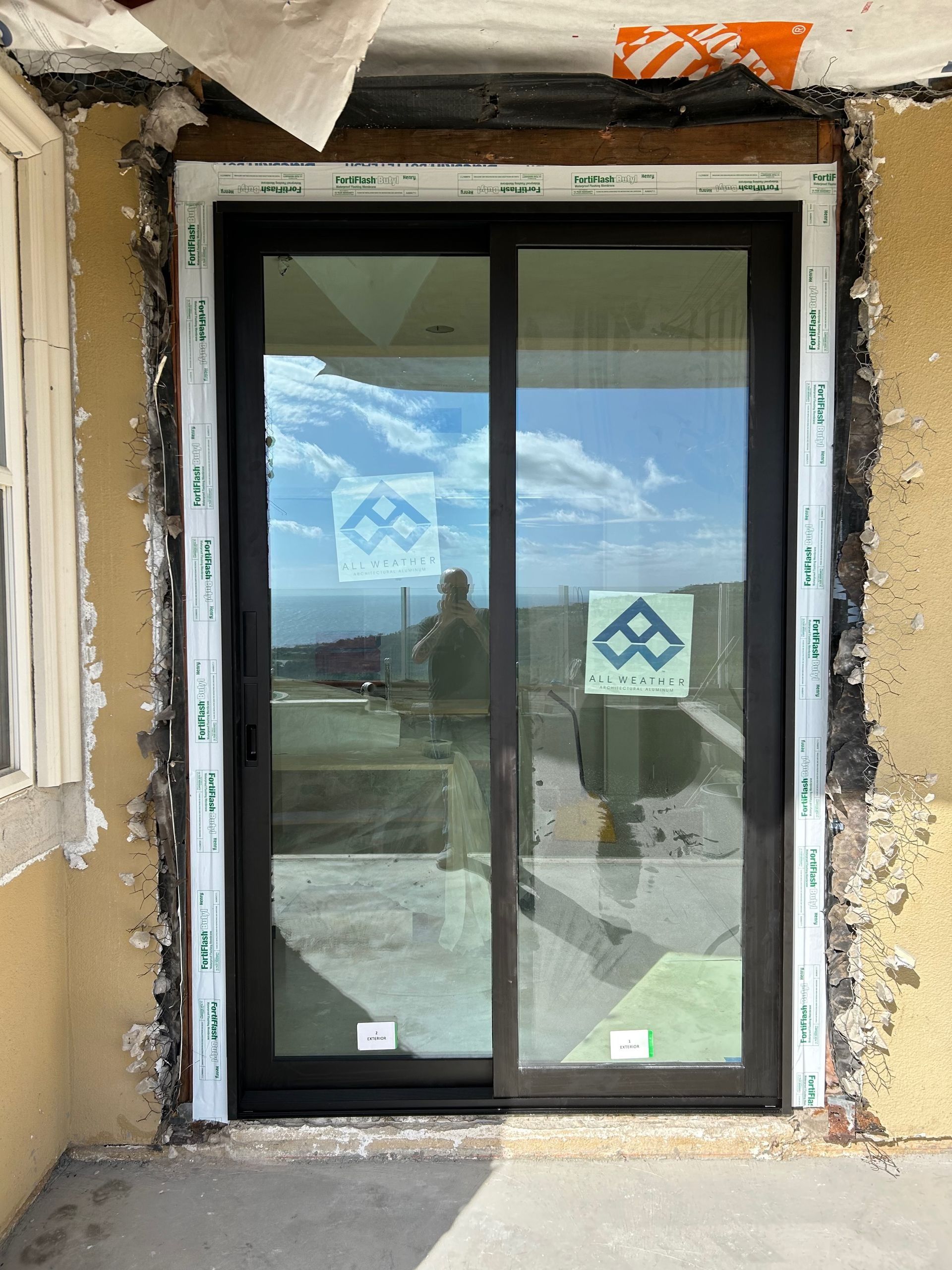New black sliding glass door installed in a rough opening of a building with visible construction materials.