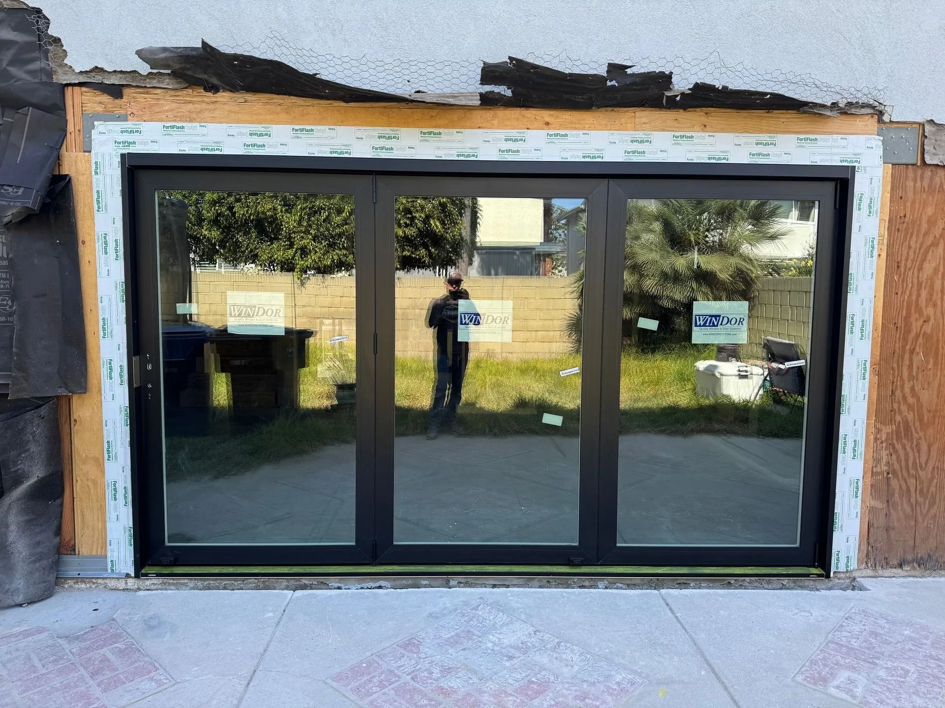 Black trifold door with glass panels in a home under construction. A person is reflected in the glass.