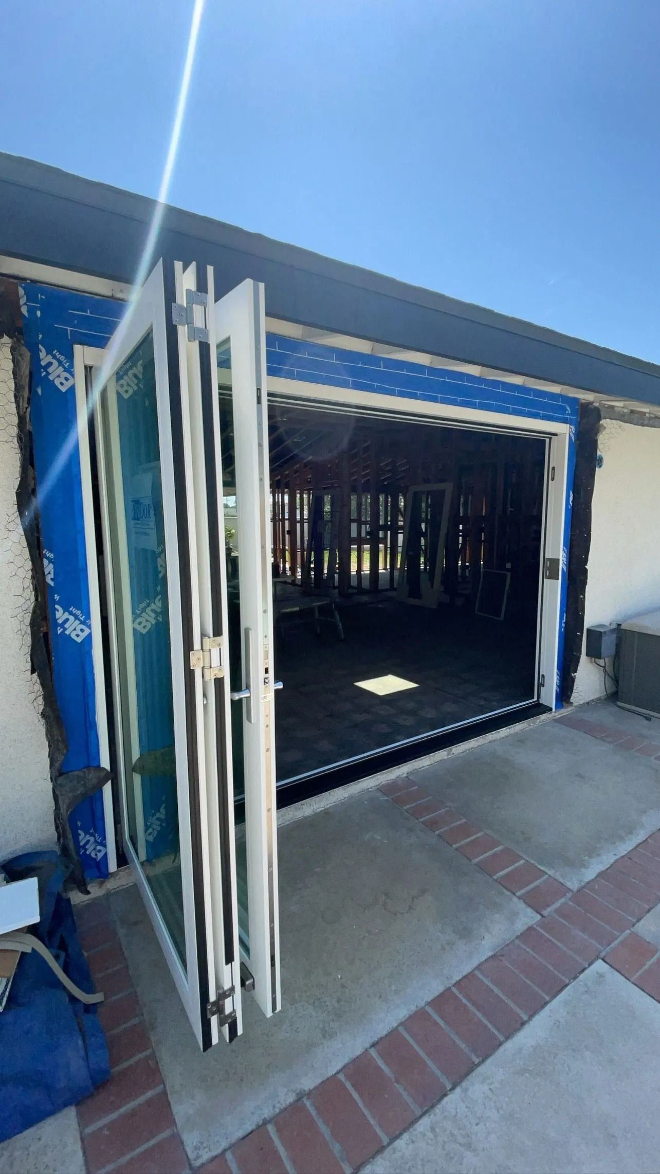 Exterior view of bi-fold doors, partially open, revealing a room under construction; blue protective covering visible.