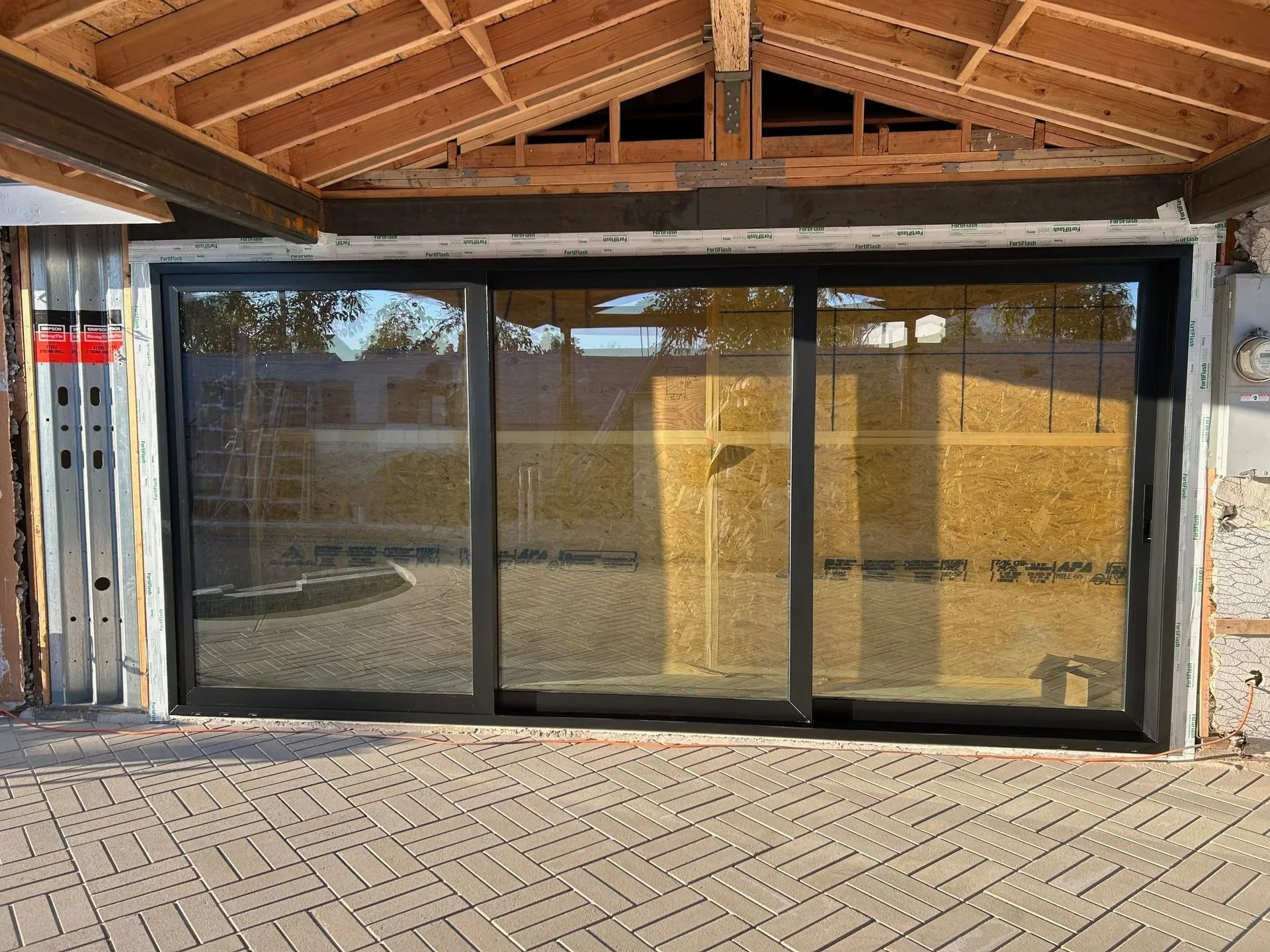 Exterior view of a three-panel sliding glass door framed by dark trim. The building is under construction.