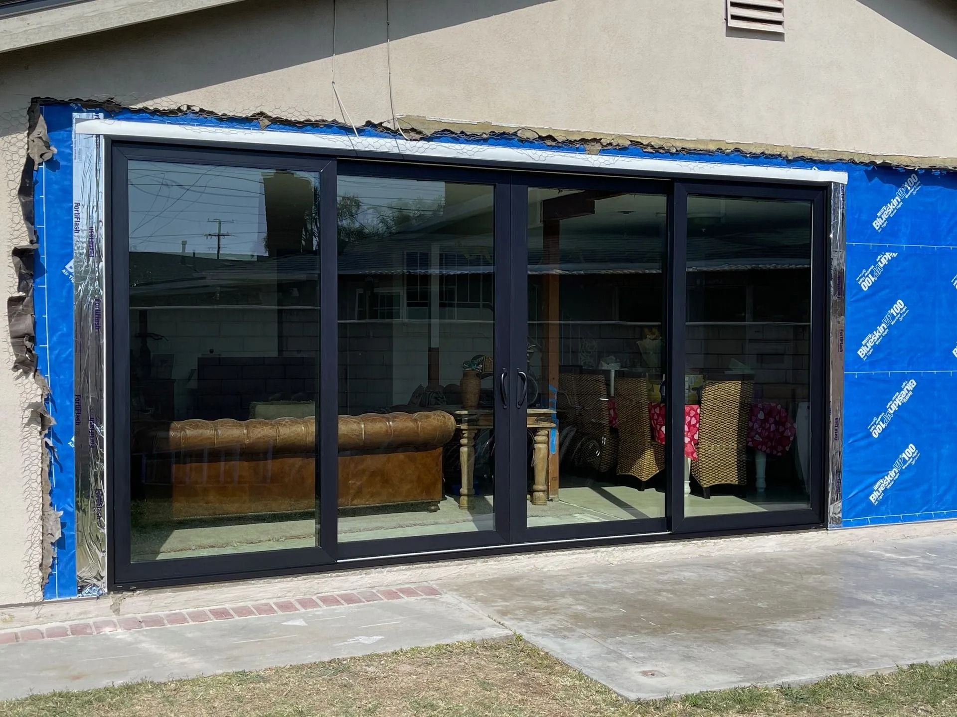 Black framed sliding glass doors installed on a home, surrounded by blue sheeting and concrete.