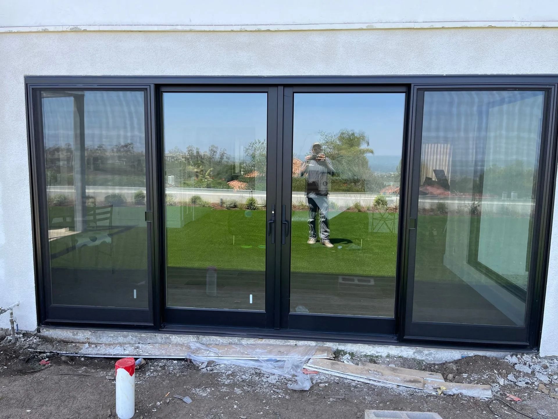 Black-framed glass sliding doors reflecting a person and yard. Installed in a white building.