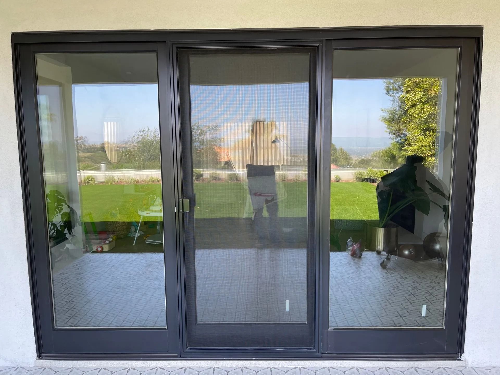 Black-framed sliding glass doors with screen, open to a patio with lawn, trees, and sky.