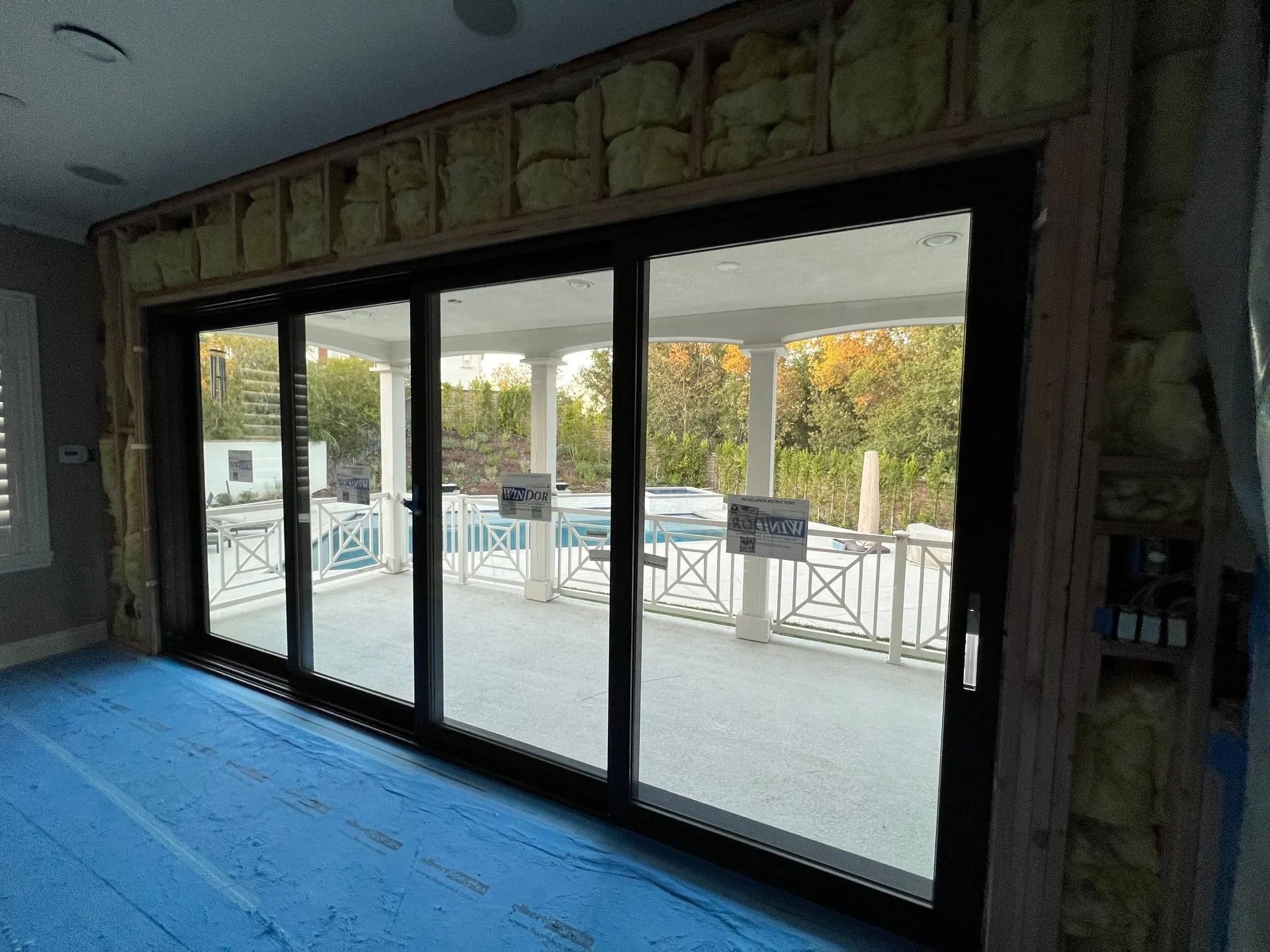 Four-panel sliding glass door opens to a patio with a pool; interior is under construction with insulation visible.