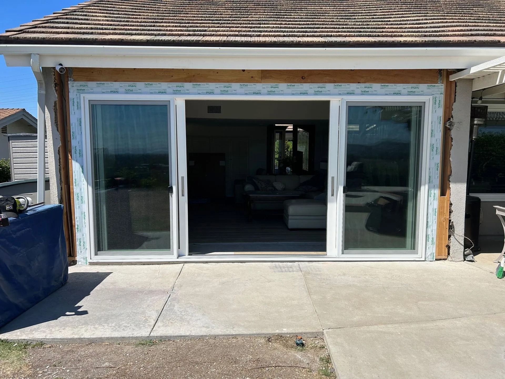 Sliding glass doors on a patio, under construction, with visible blue wrap, and a glimpse of the interior.