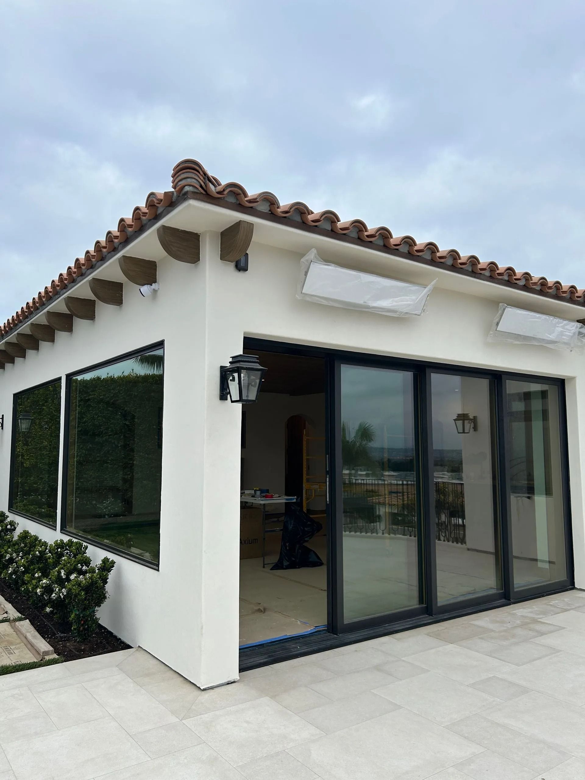 White stucco building with black-framed sliding glass doors, terracotta roof, and outdoor tiled patio.