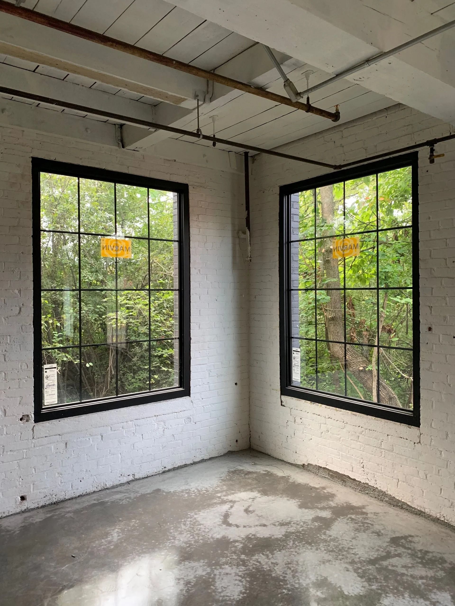 Corner room with two black-framed windows, white brick walls, and a gray concrete floor.