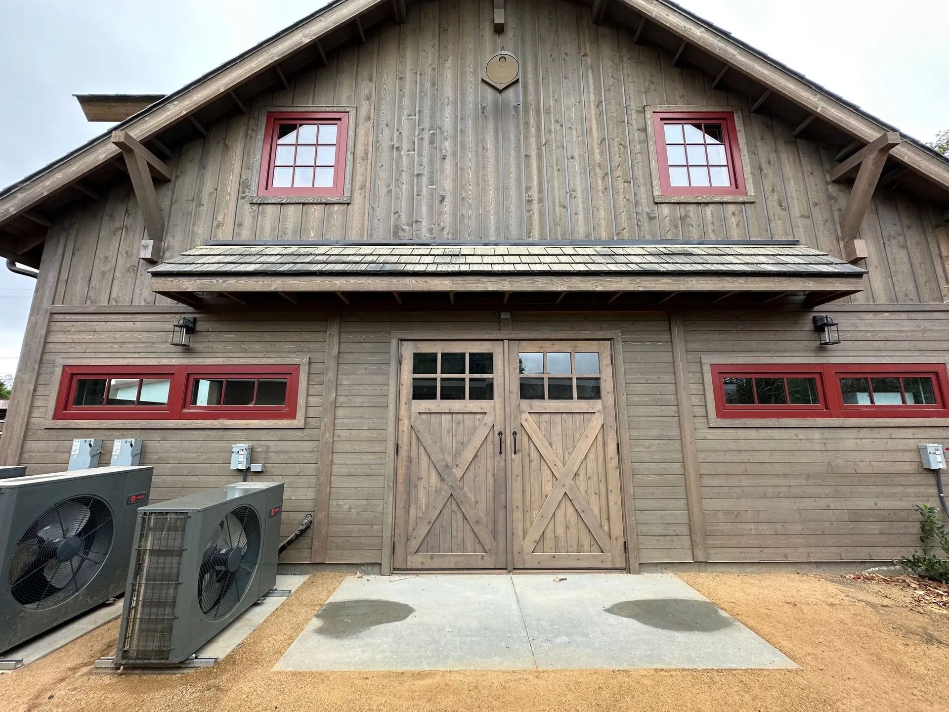 Wooden building with red-framed windows and double doors. Two large grey machines stand at the building’s left side.