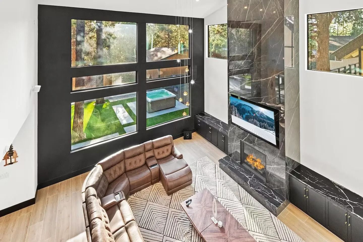 Modern living room with large windows, leather sectional, fireplace, and scenic outdoor view.