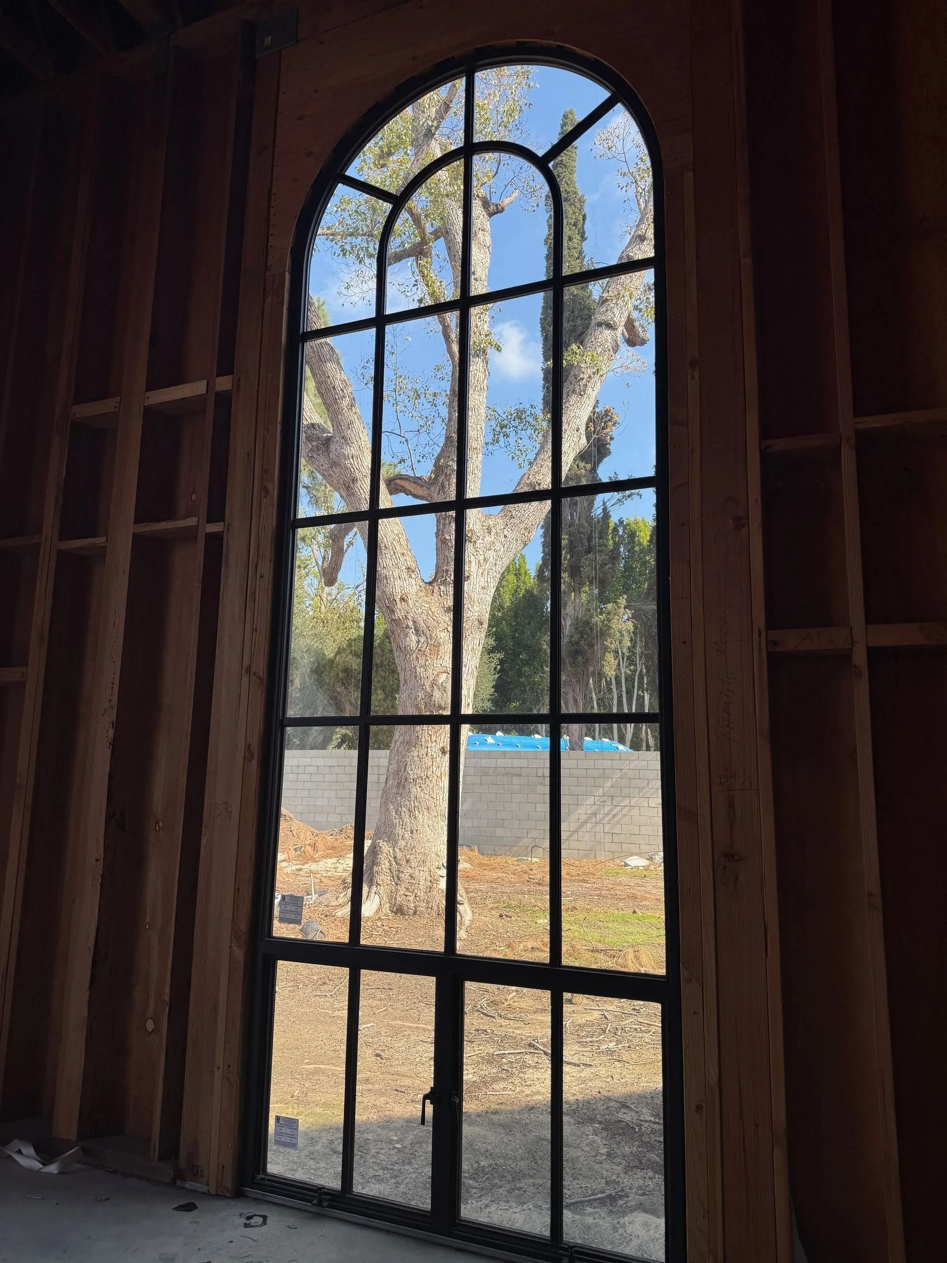 Tall arched window framed in black, revealing a tree and blue sky through the glass.