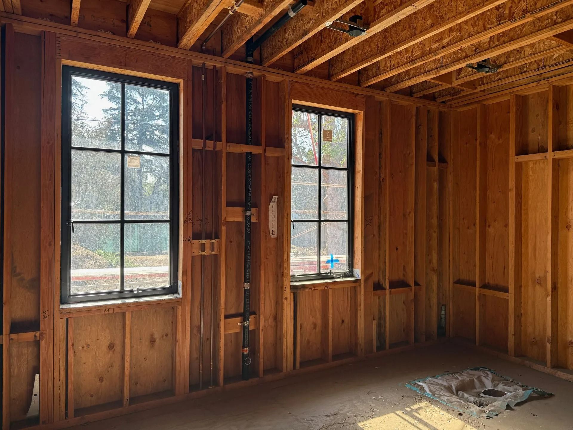 Interior of a room under construction with two black-framed windows and exposed wooden framing.