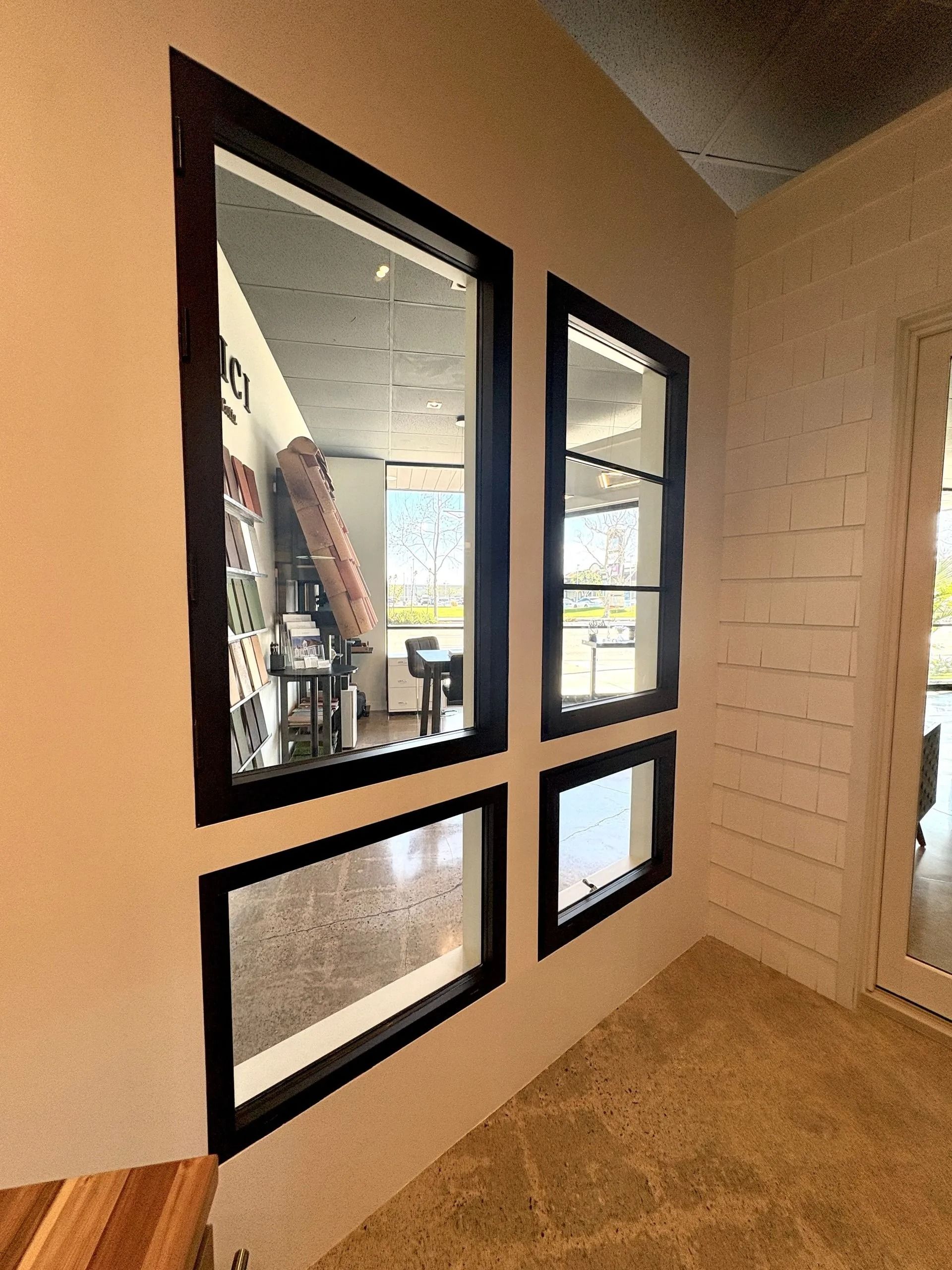 Windows with dark frames on a beige wall, reflecting interior and exterior views.