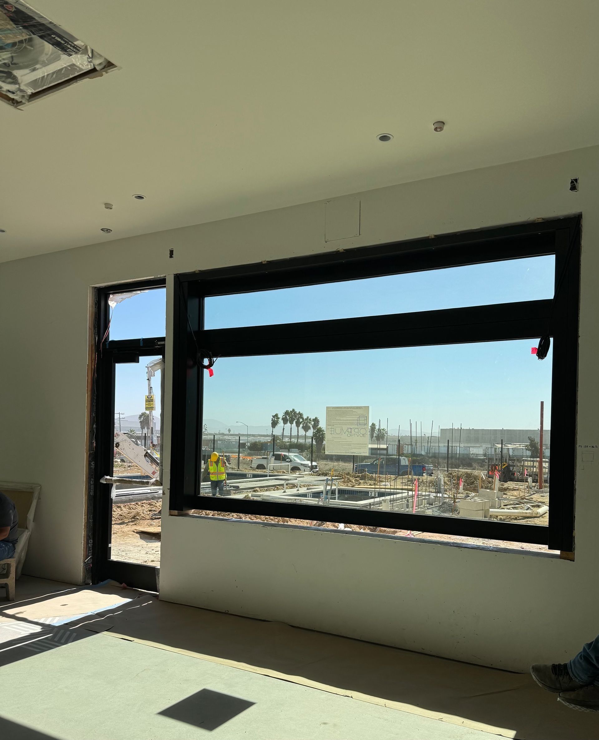 Interior view of a building under construction, featuring a large window with a construction site visible.