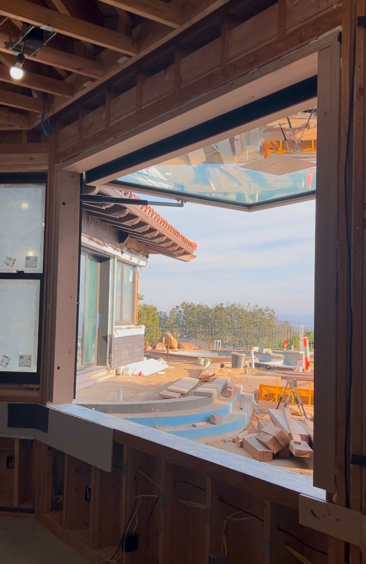 Open window in a wood-framed building, overlooking a construction site with a view of hills and a partially built pool.