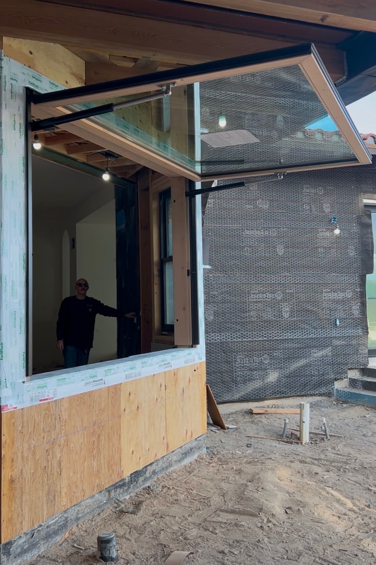 A window, open upward, on a building under construction. Man stands inside.