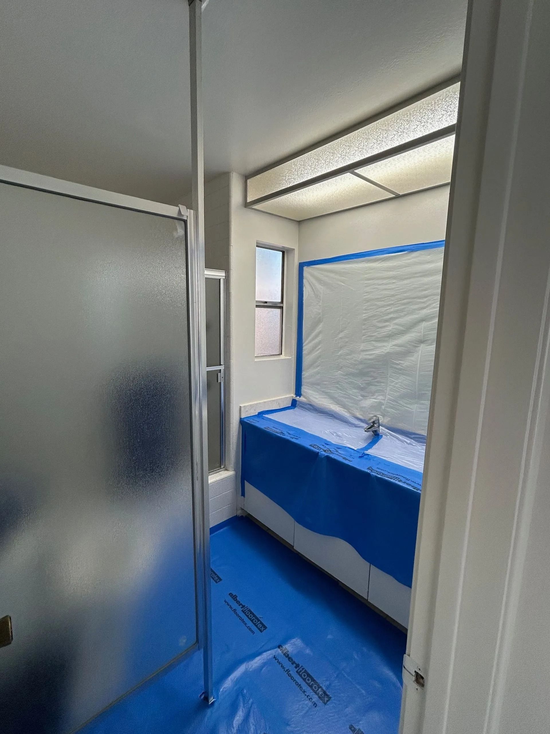 Bathroom with a frosted glass shower door, bathtub covered in blue tarp, and blue floor covering.