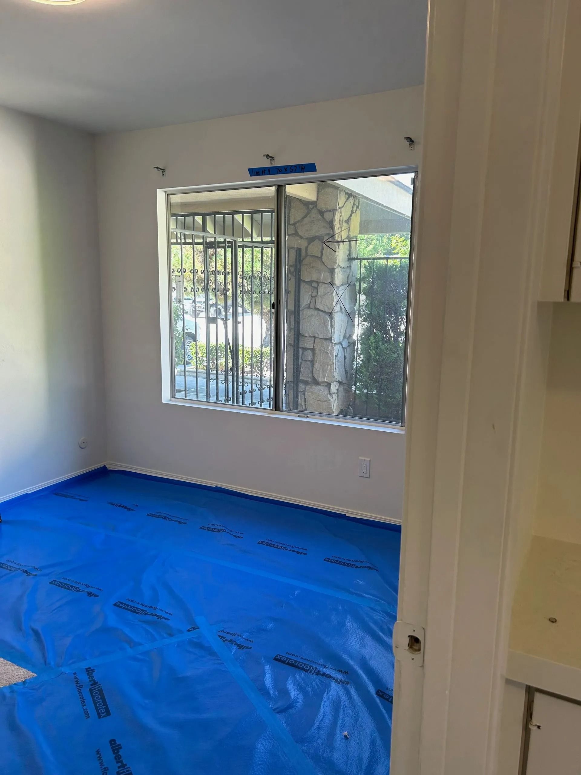 Empty room with blue floor covering, window with security bars, and white walls.