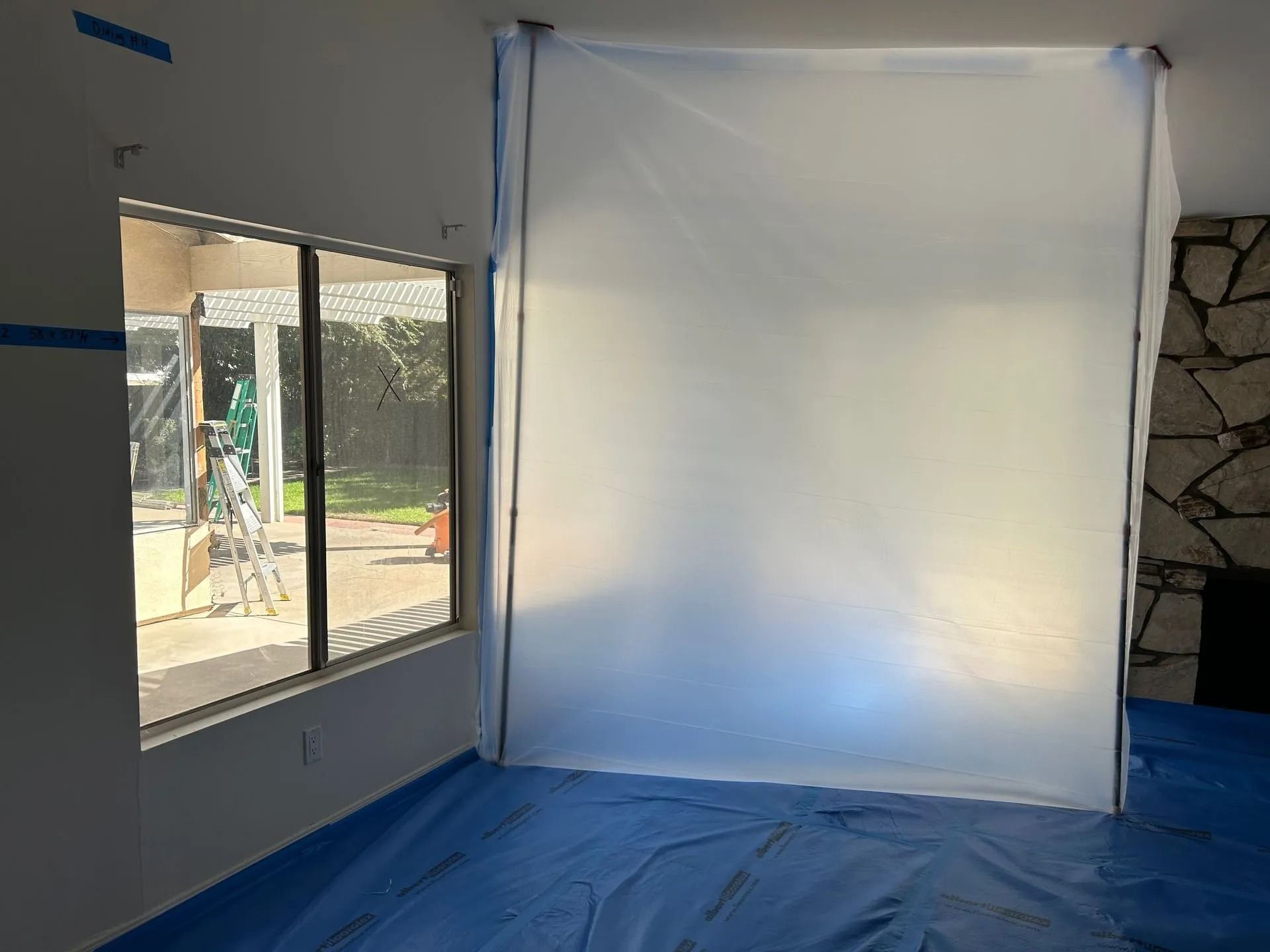 Room prepared for painting; plastic sheeting covers walls, window, and floor.