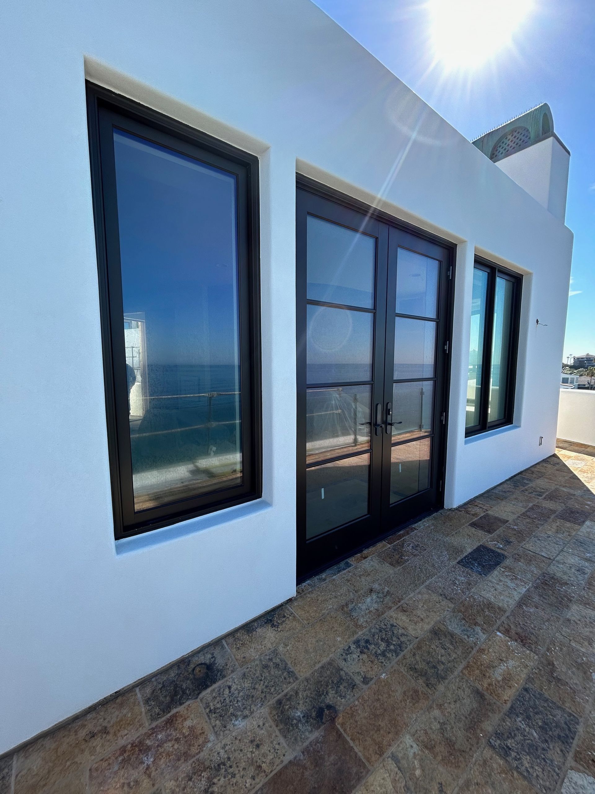 Exterior of white building with black-framed windows and doors, facing ocean.