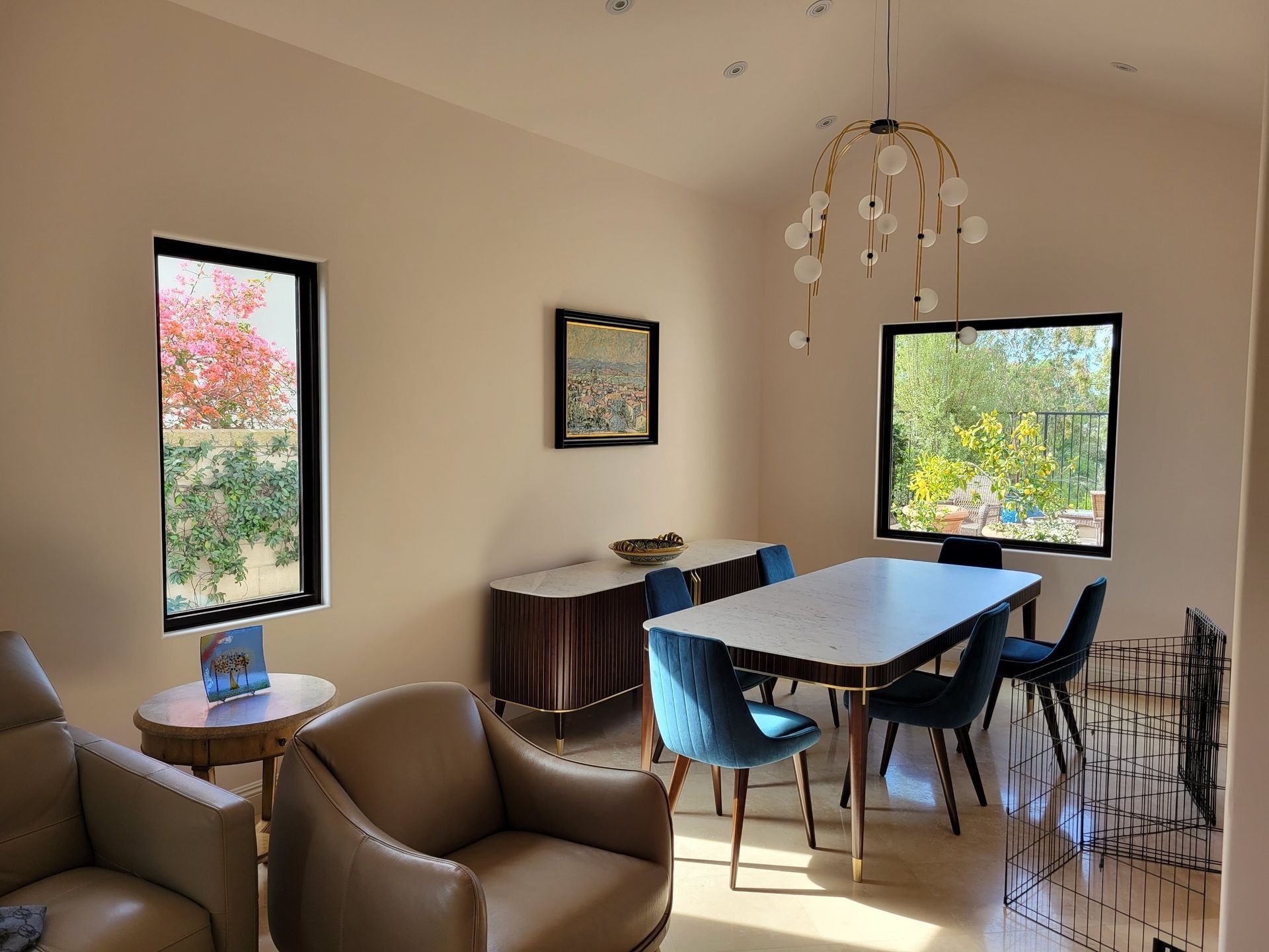 Dining room with marble table, blue chairs, gold chandelier, and cream walls.
